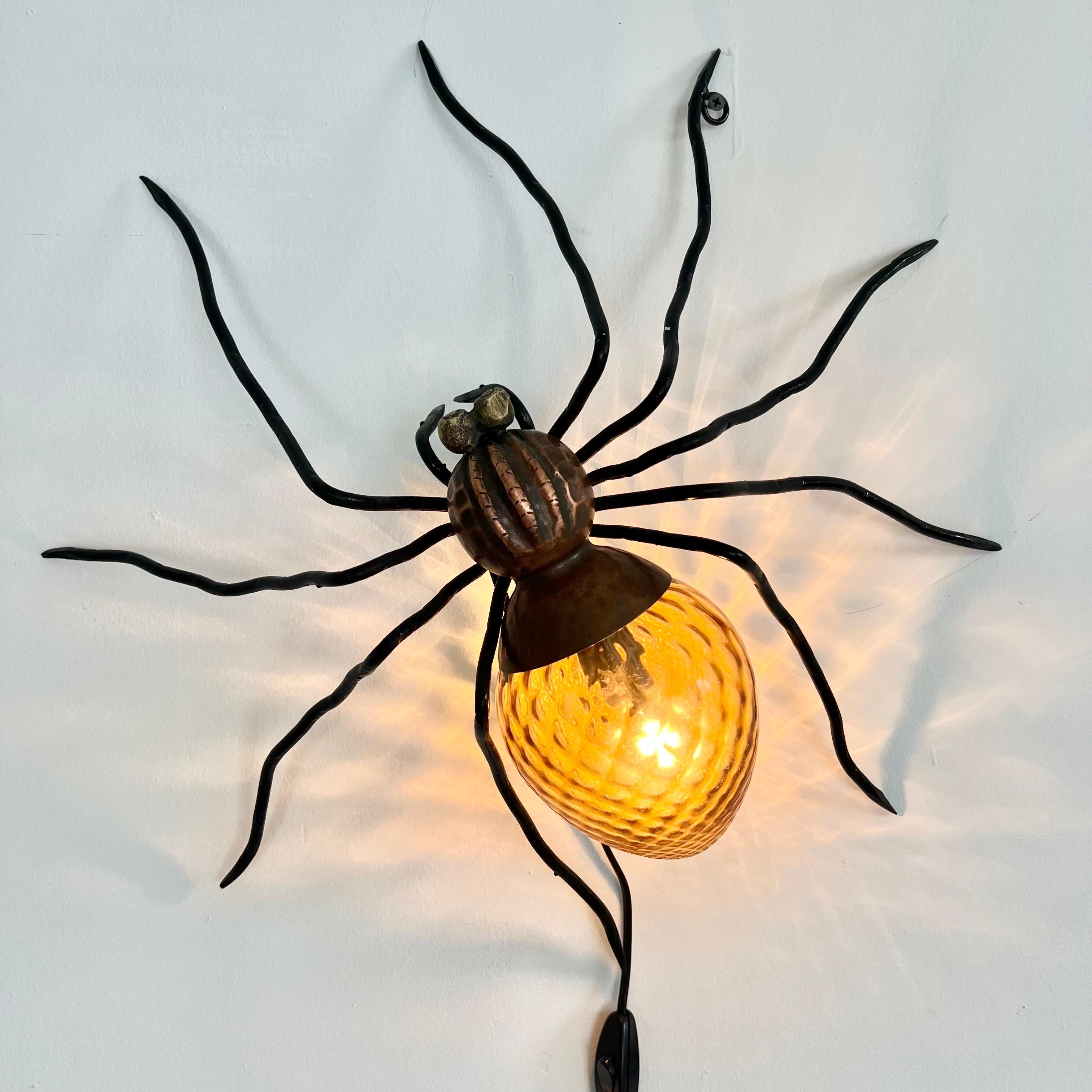 Unique copper and metal spider sconce handmade in Italy. Great presence and detail. Hammered copper body with black head and slender long legs. The abdomen is a beautiful amber glass globe with a honeycomb design. Eye catching lines and coloring.