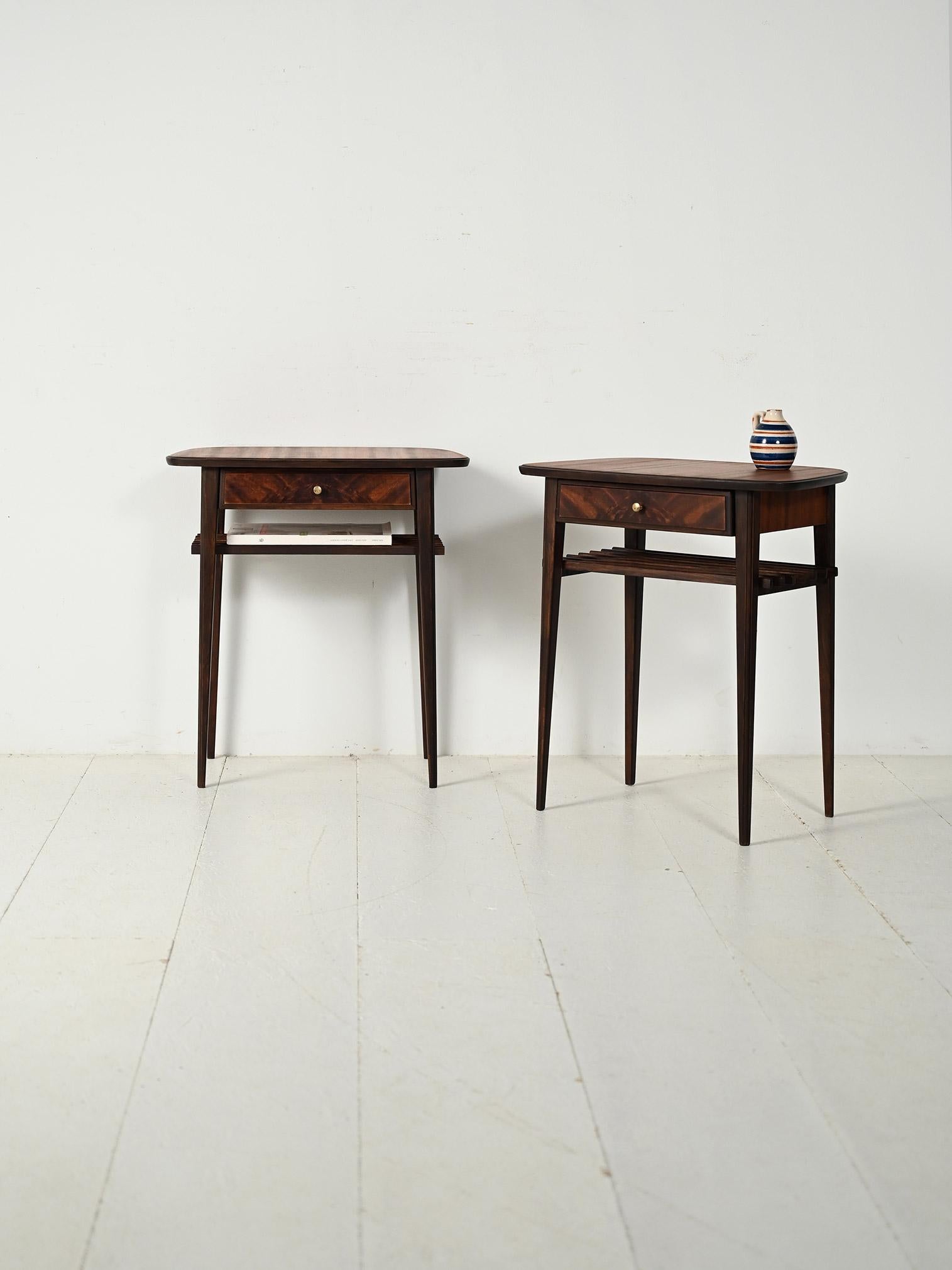 Coppia di comodini scandinavi anni '50 in mogano, cassetto con pomolo in ottone e mensola portariviste a listelli; top dalla forma organica.

Linee leggere e proporzioni affusolate per una coppia di comodini scandinavi anni '50 in Mogano. Piano