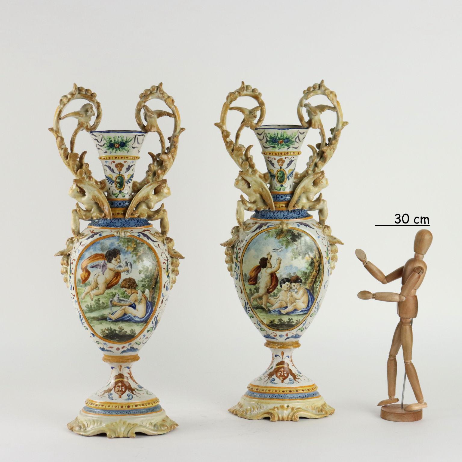 Coppia di anfore in maiolica policroma con motivi a grottesche. Riserve da ambo i lati decorate con motivi allegorico-mitologici. Le anse laterali, molto insellate, sono sorrette da figure alate. Marchio della manifattura assente.