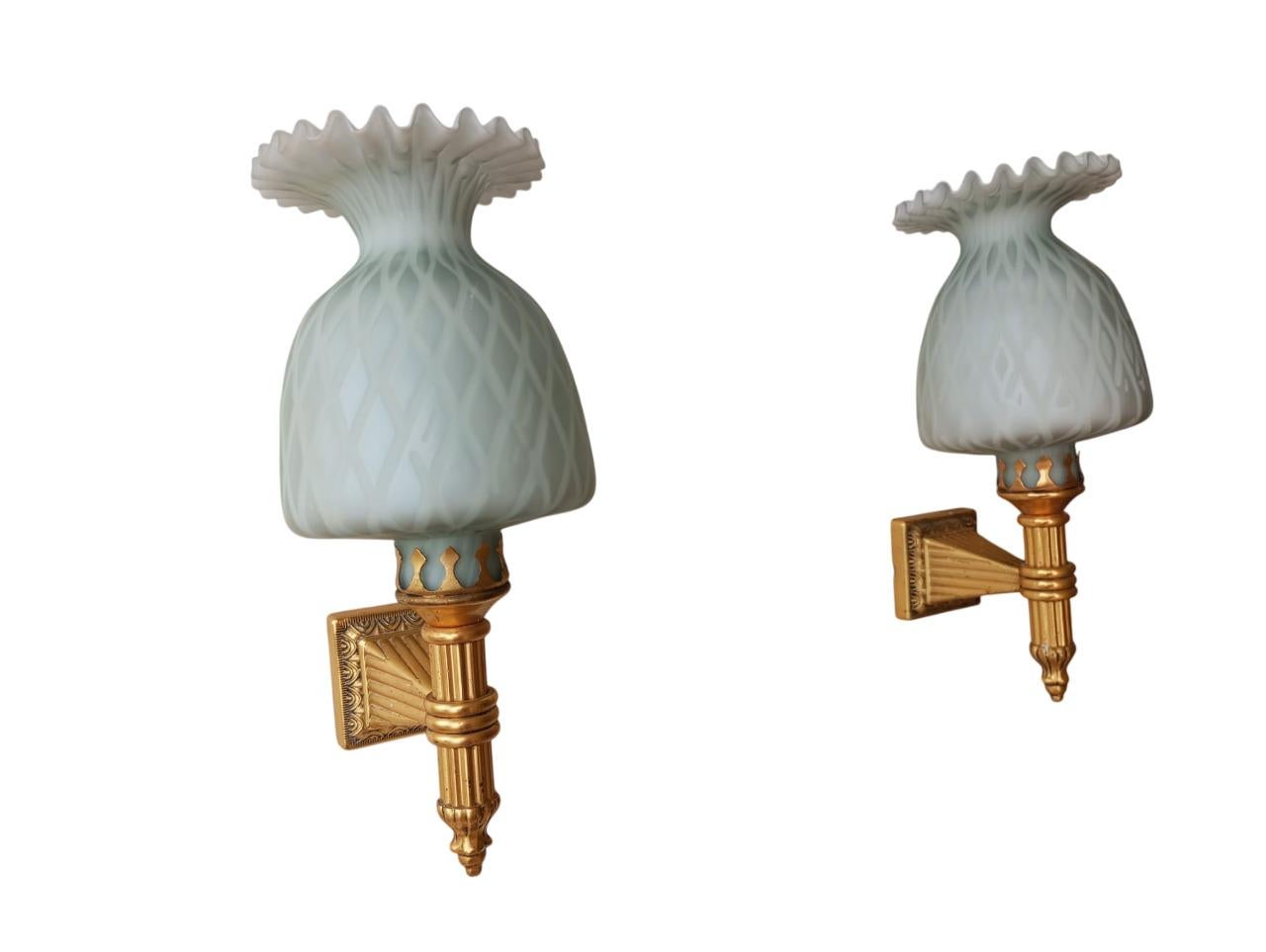 Appliques Francesi anni ’70 in ottone dorato e vetro satinato, hanno  la base quadrata con incisioni ornamentali mentre il braccio in ottone dorato con un design decorativo ricco di dettagli e motivi in rilievo, che richiama le torce decorative. Il