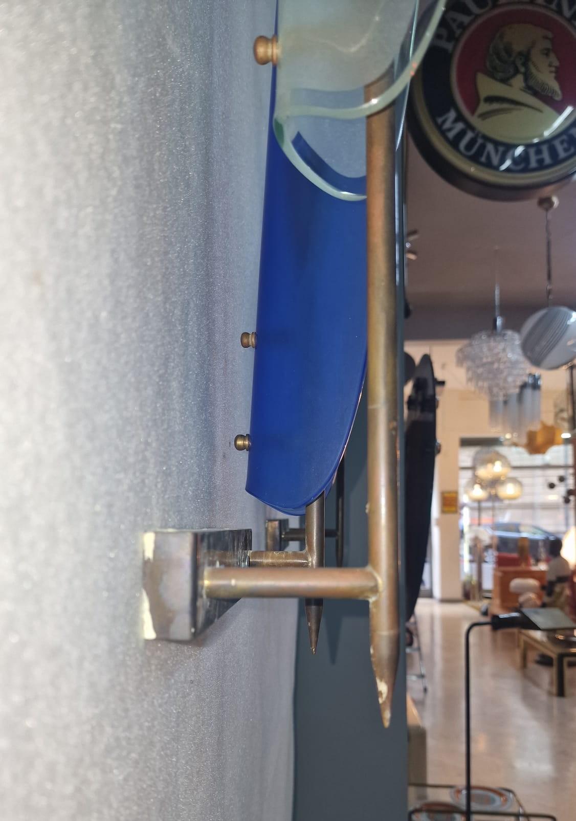 Elegante e particolare coppia di applique prodotti da Cristal Art con struttura in metallo e doppio vetro in due colori diversi: uno blu e l'altro incolore.
In questo specifico modello di applique le lampadine sono a vista e la parte in vetro è