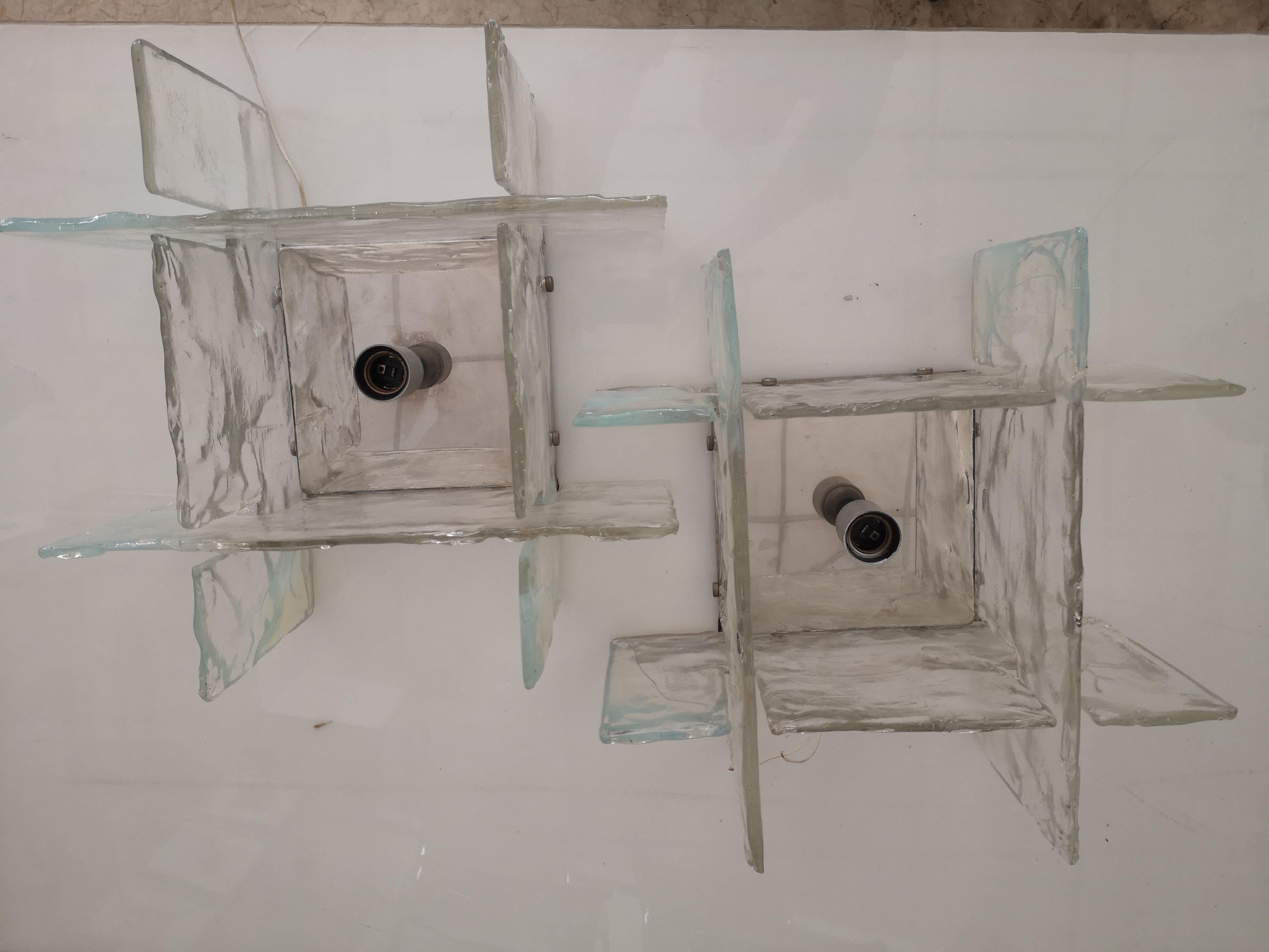 Coppia di applique da parete in vetro di Murano disegnate da Carlo Nason e prodotte da Mazzega negli anni '60. La struttura delle applique è in acciaio cromato e hanno quattro sfaccettature in vetro di Murano che diffondono la luce. Funziona con una