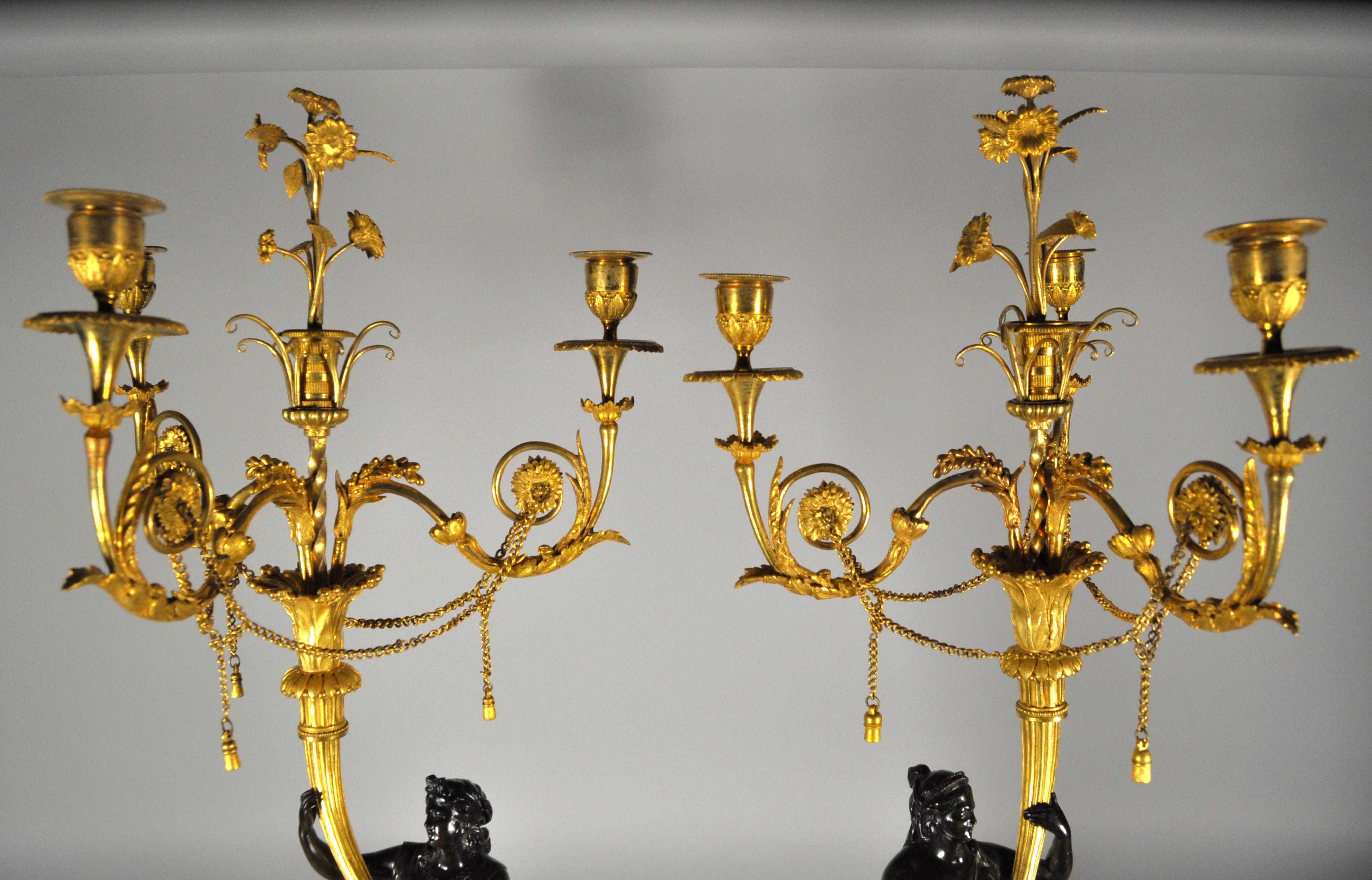 Coppia di grandi ed eleganti candelabri francesi con vestali in bronzo brunito che reggono tra le mani delle cornucopie in bronzo dorato, dalle quali si aprono i quattro bracci del candelabro: uno centrale decorato con bouquet di fiori e tre bracci