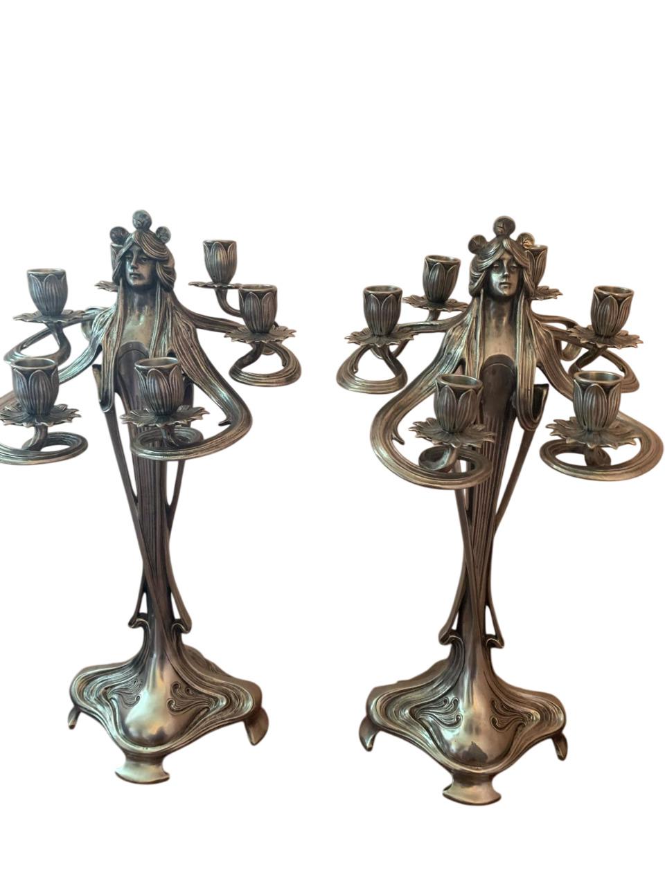Elegante coppia di candelabri in peltro argentato in stile Art Nouveau, disegnati da Achille Gamba.
Germania  inizi XX secolo.
Ogni candelabro rappresenta una figura femminile stilizzata dai lunghi capelli fluenti, che si diramano come sei braccia