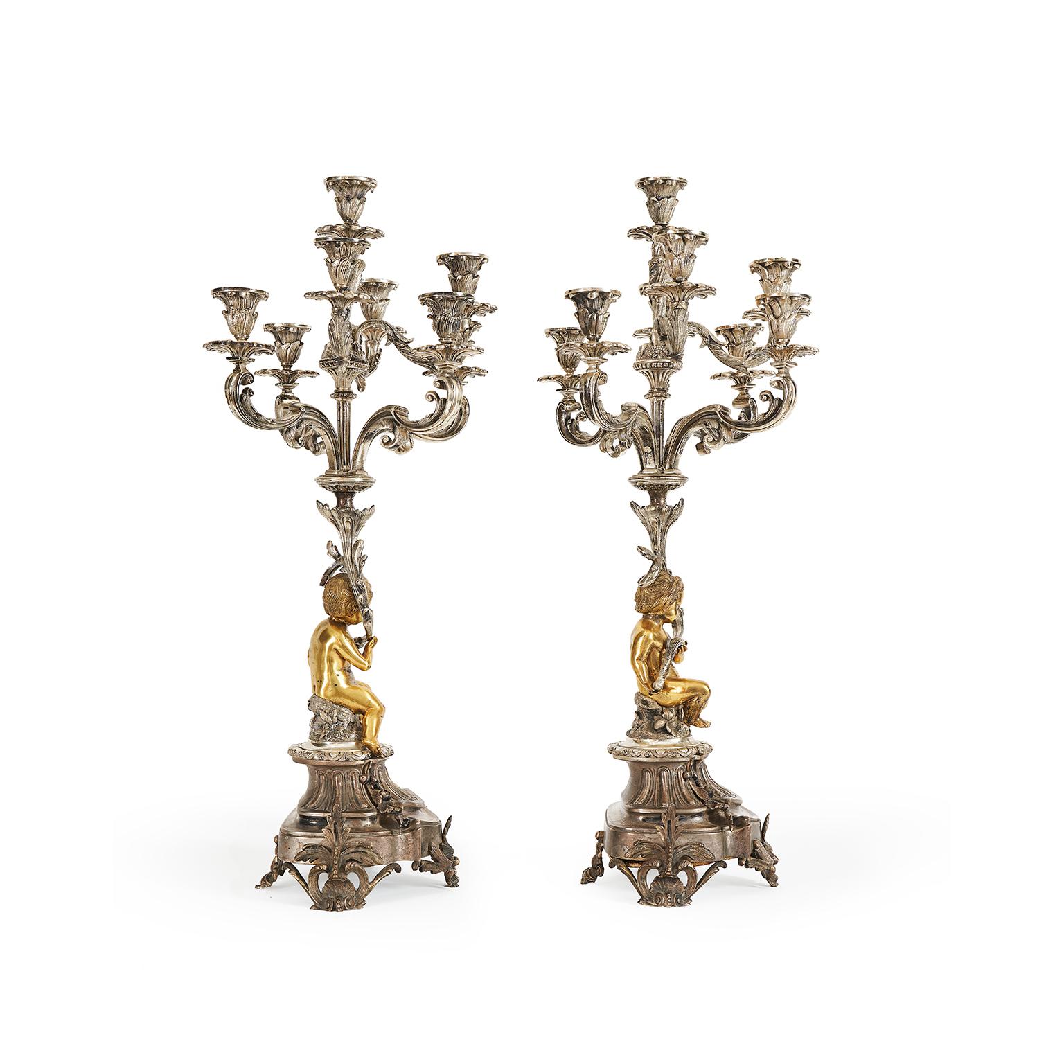 Coppia Di Candelabri Da Tavolo In Bronzo Argentato E Dorato A Otto Bracci della seconda metà del 1800 realizzati con un’esuberante decorazione rocaille ricca di curve sinuose e motivi vegetali retti da due angeli dorati. I due imponenti candelieri