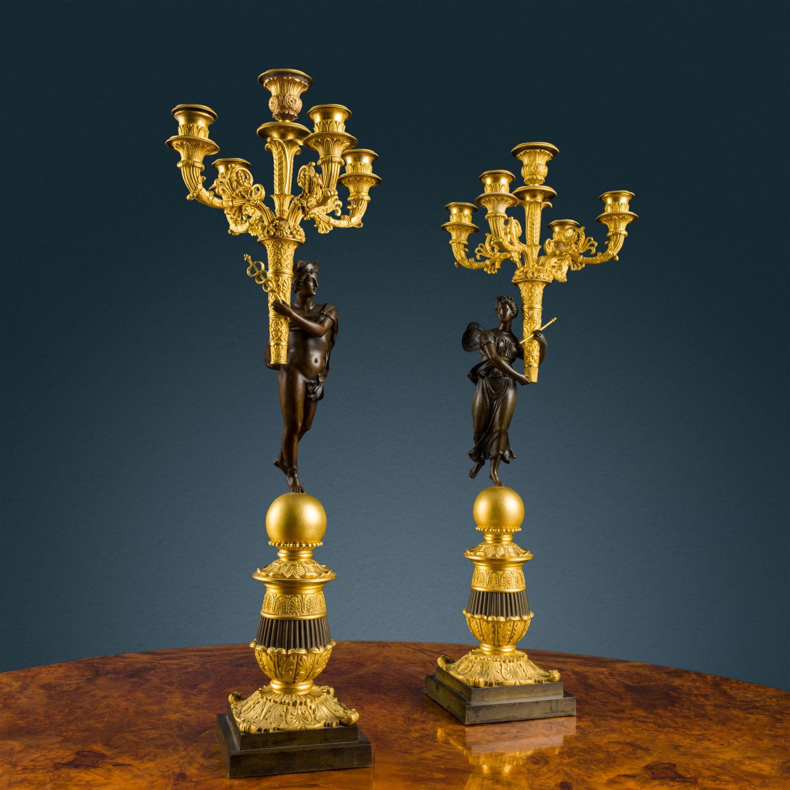 Paire de candélabres en bronze partiellement doré et bruni. Base à gradins d'où part le corps tourné et ciselé avec des motifs de feuilles et d'anthémis, au sommet de laquelle se trouve une sphère dorée formant le support des deux sculptures en