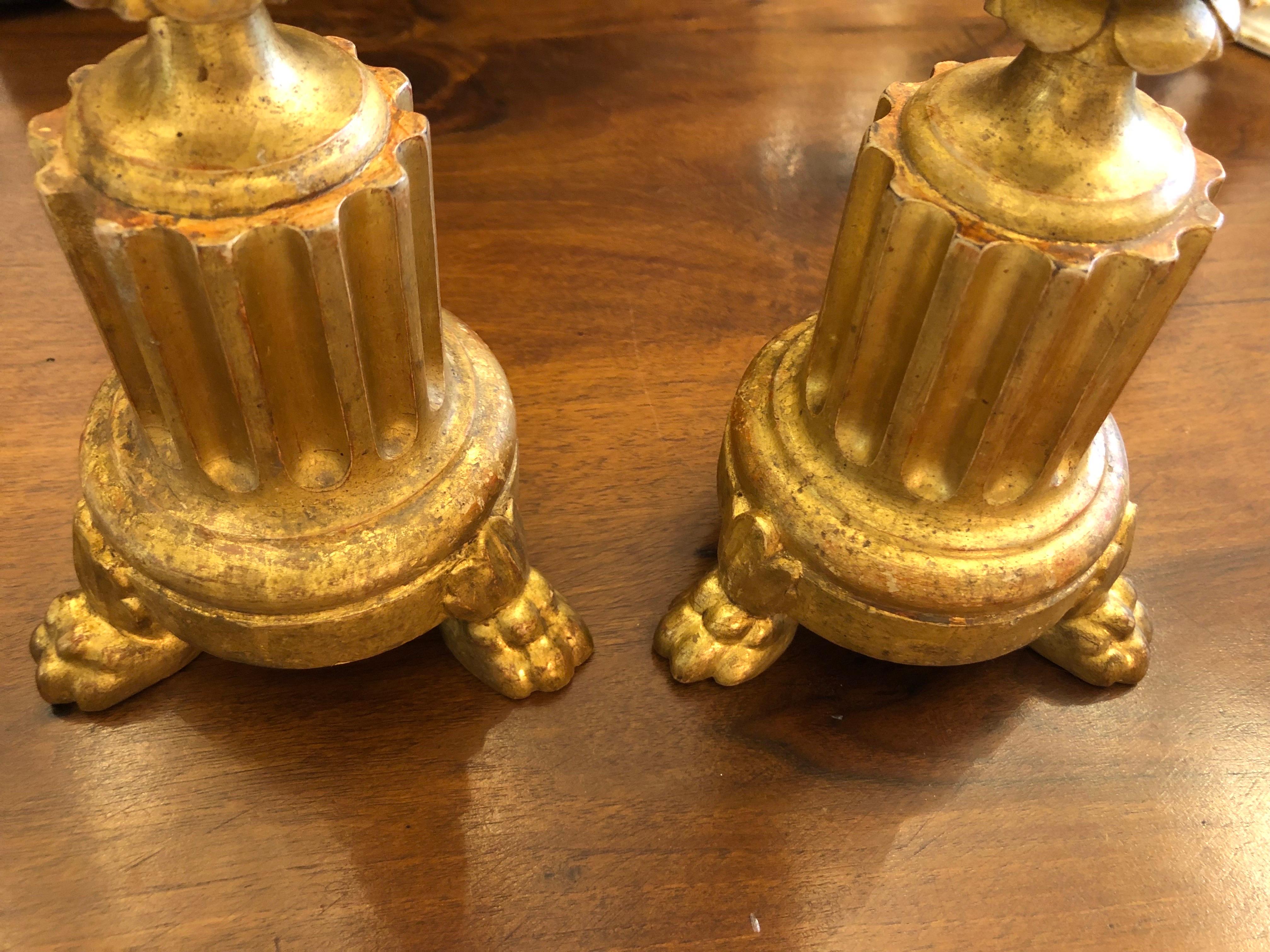 Pair of Carved and Gilded Wooden Candlesticks 1800, two Italian candlestick holders of circular shape, with the base decorated with grooves and carved with plant motifs with acanthus leaves and beading. They rest on three feet with zoomorphic