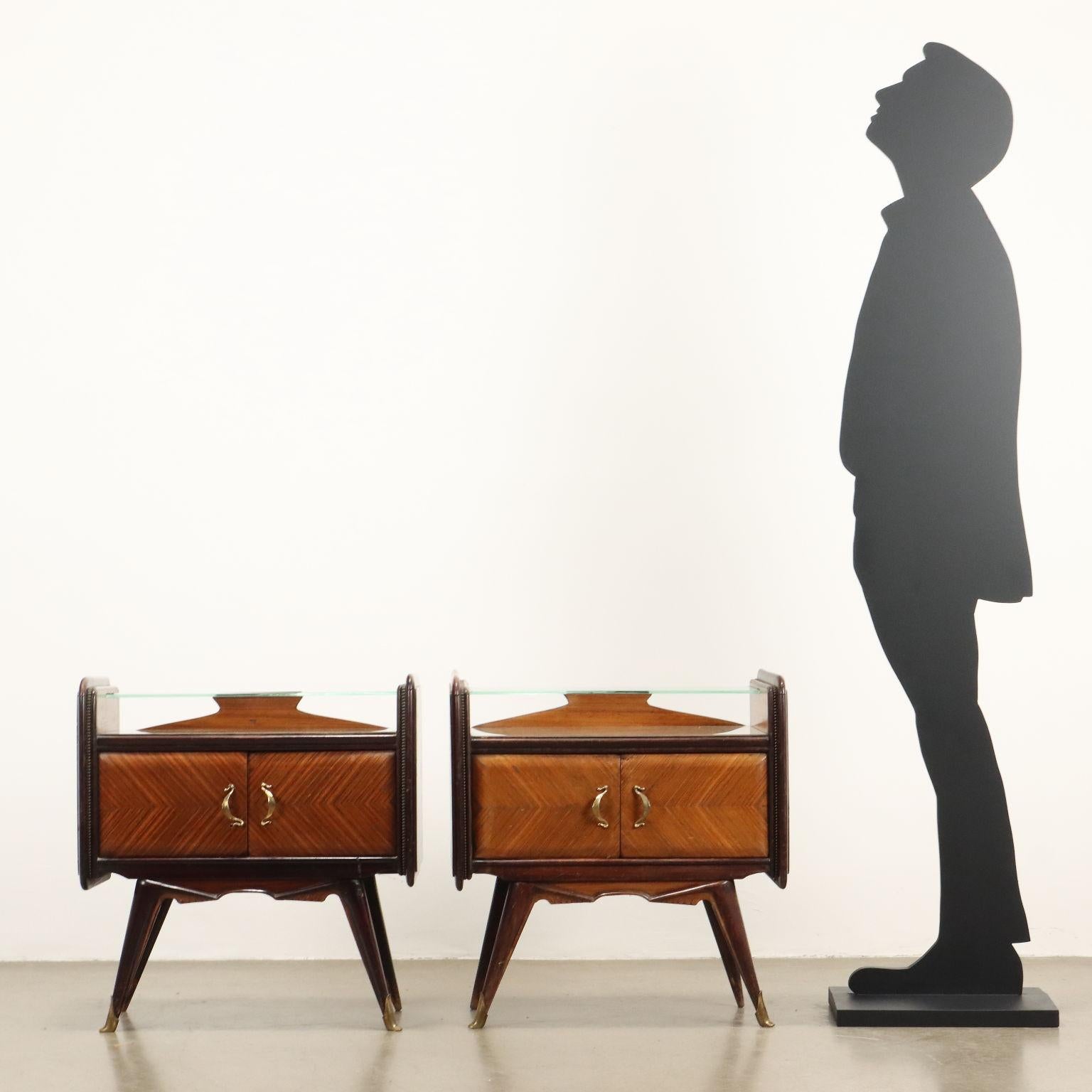 Tables de chevet avec portes battantes, bois plaqué de bois exotique, plateau en verre rétro-traité et tablette en verre transparent, fleurons en laiton.