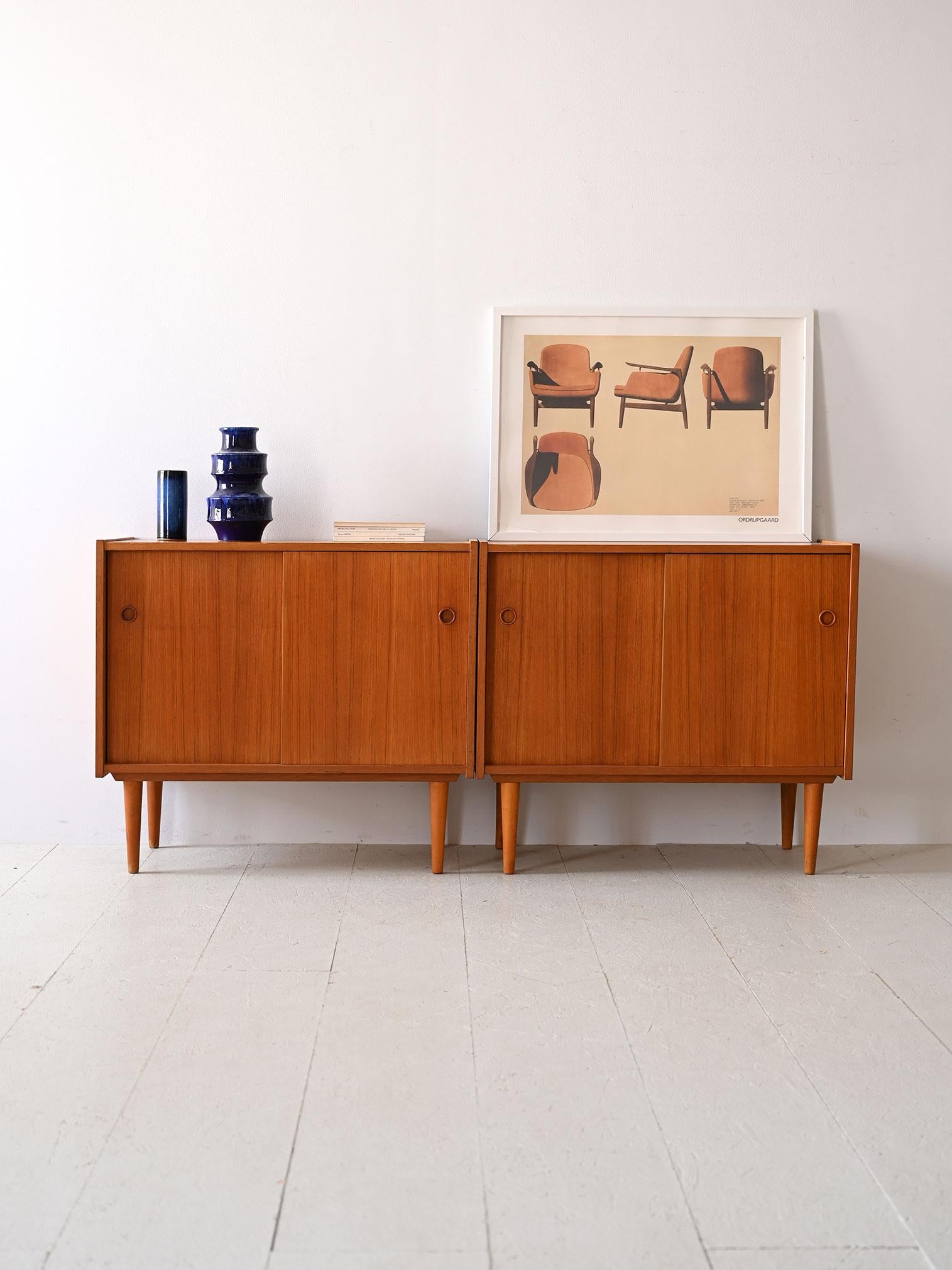 Vintage teak sideboards with sliding doors.

This pair of 1960s cabinets reflects Scandinavian design in its purest essence. Each cabinet features a compartment with a shelf inside, optimal for organizing and hiding everyday items.
Smooth wood