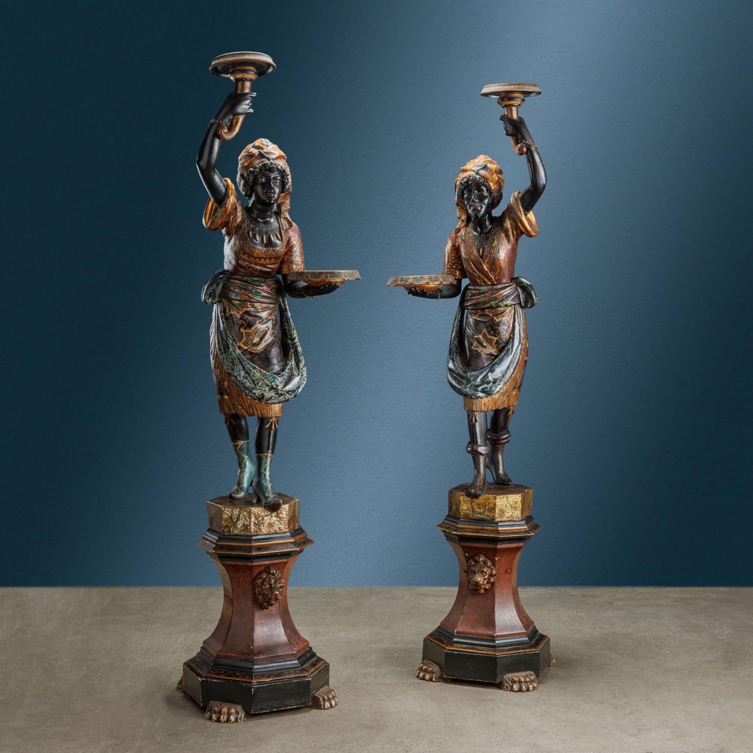 Pair of torch-holding sculptures depicting two Venetian Moors, one female figure and the other male. In a mirrored position of slight advancement, they hold a tray in one hand while in the other, raised above their heads, a cornucopia with