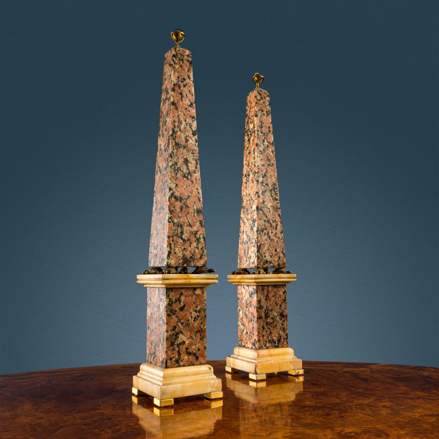 Coppia di obelischi in Granito Rosso sormontati da due globi terrestre e celeste in bronzo dorato. Gli obelischi poggiano su due plinti sempre in granito con base e capitello in marmo Giallo di Siena poggianti su piedini in bronzo dorato; i due