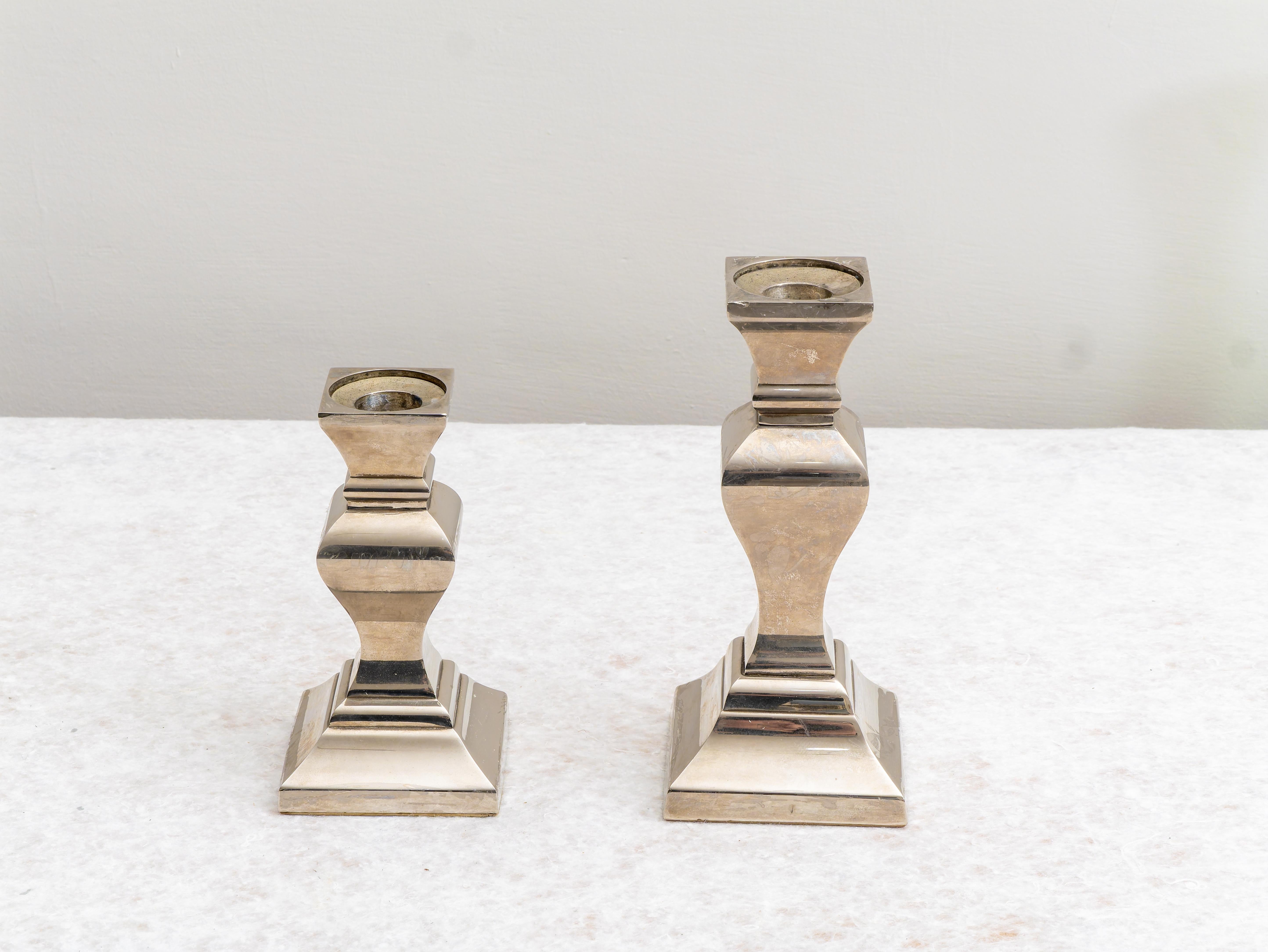 Coppia di Portacandele in metallo placcati in argento, XX secolo.  
Coppia di Portacandele in metallo placcato in argento con forme moderne. Le condizioni sono eccellenti, può presentare lievi segni del tempo dovuti all'età e all'utilizzo.  
Il