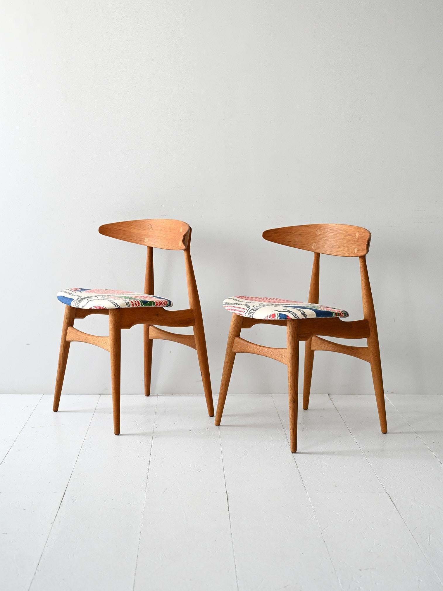 Iconic 1950s Danish chairs with oak frame and seat upholstered in signature fabric by Josef Frank.

Pair of chairs model CH33 designed by Hans J. Wegner and manufactured by Carl Hansen & Søn. The frame is solid oak, with organic lines typical of