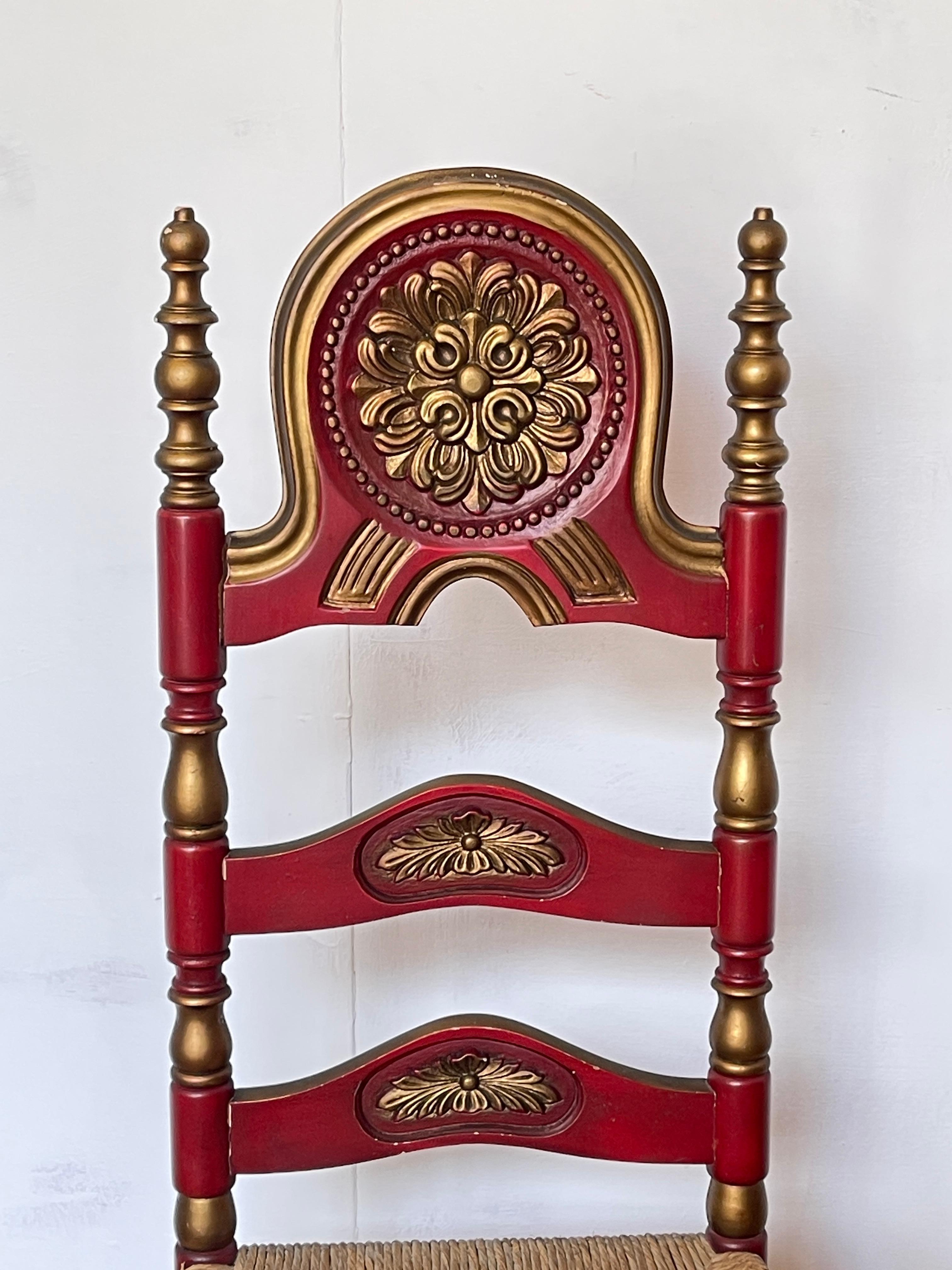 Pair of handcrafted wooden chairs, featuring a vibrant red color and golden details, represents a perfect balance of tradition and style. Featuring a sturdy frame and woven straw seat, the chairs are embellished with delicate floral carvings on the
