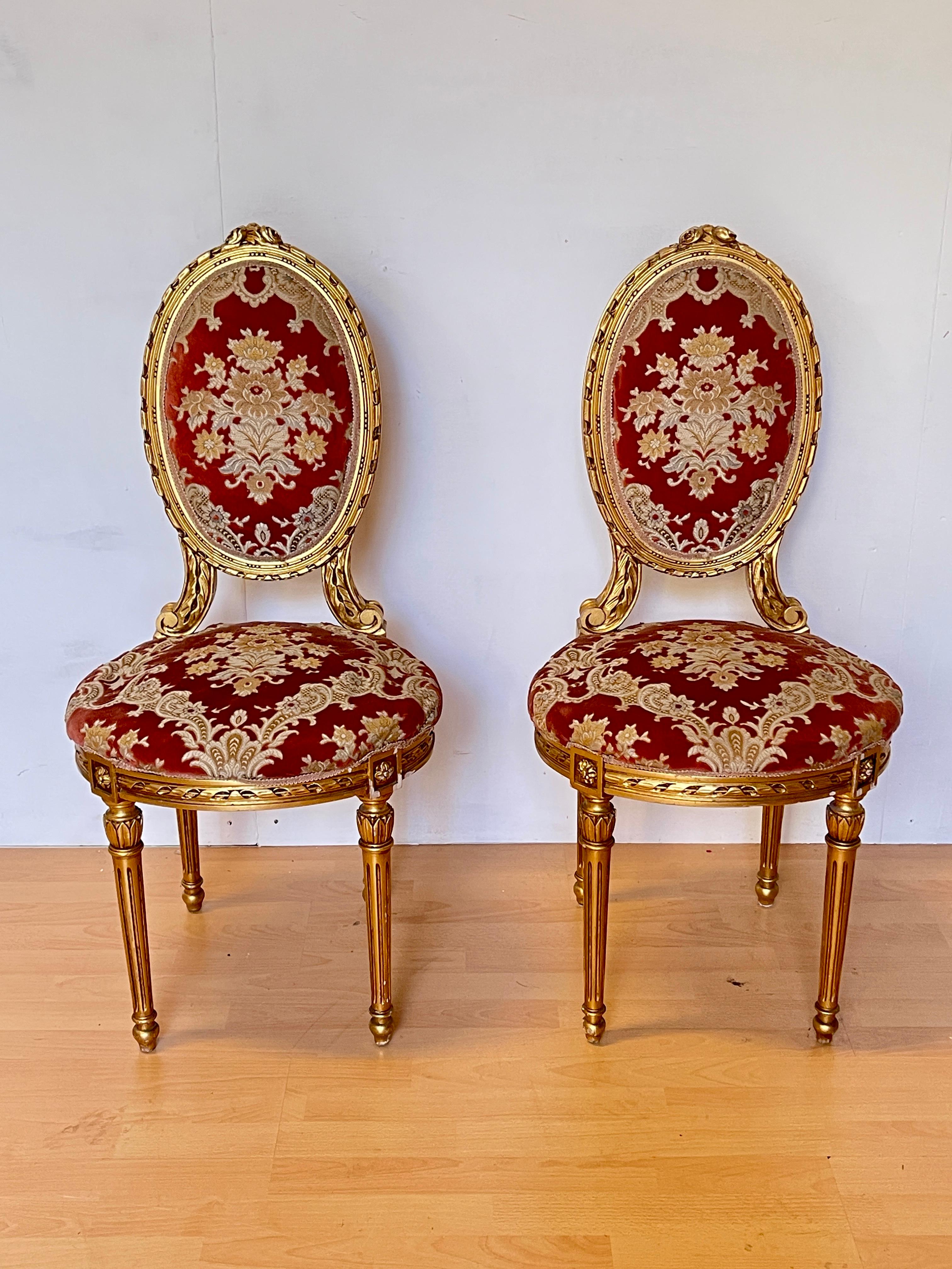 Elegant pair of Louis XVI style chairs, perfect for adding a touch of royalty to any room. These oval-backed chairs are finely carved and gilded with gold leaf, with floral details and carved rosettes on the sides. The seat and back are upholstered