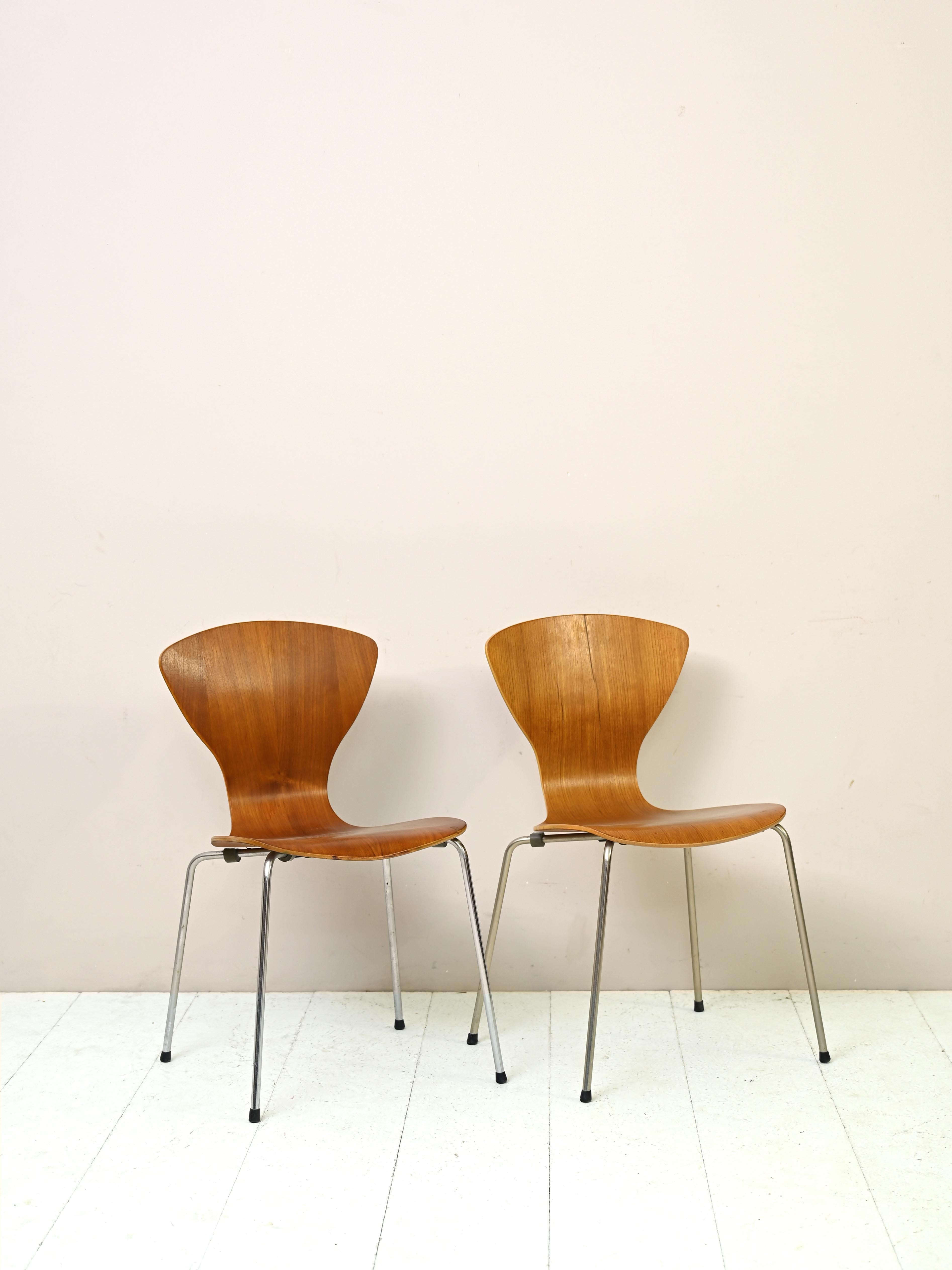 Original vintage 1960s chairs.

These elegant, minimalist chairs feature metal legs and a seat with a contoured teak back. 
The curvy lines and golden color of the teak make them timelessly beautiful Scandinavian design pieces.
Ideal for a