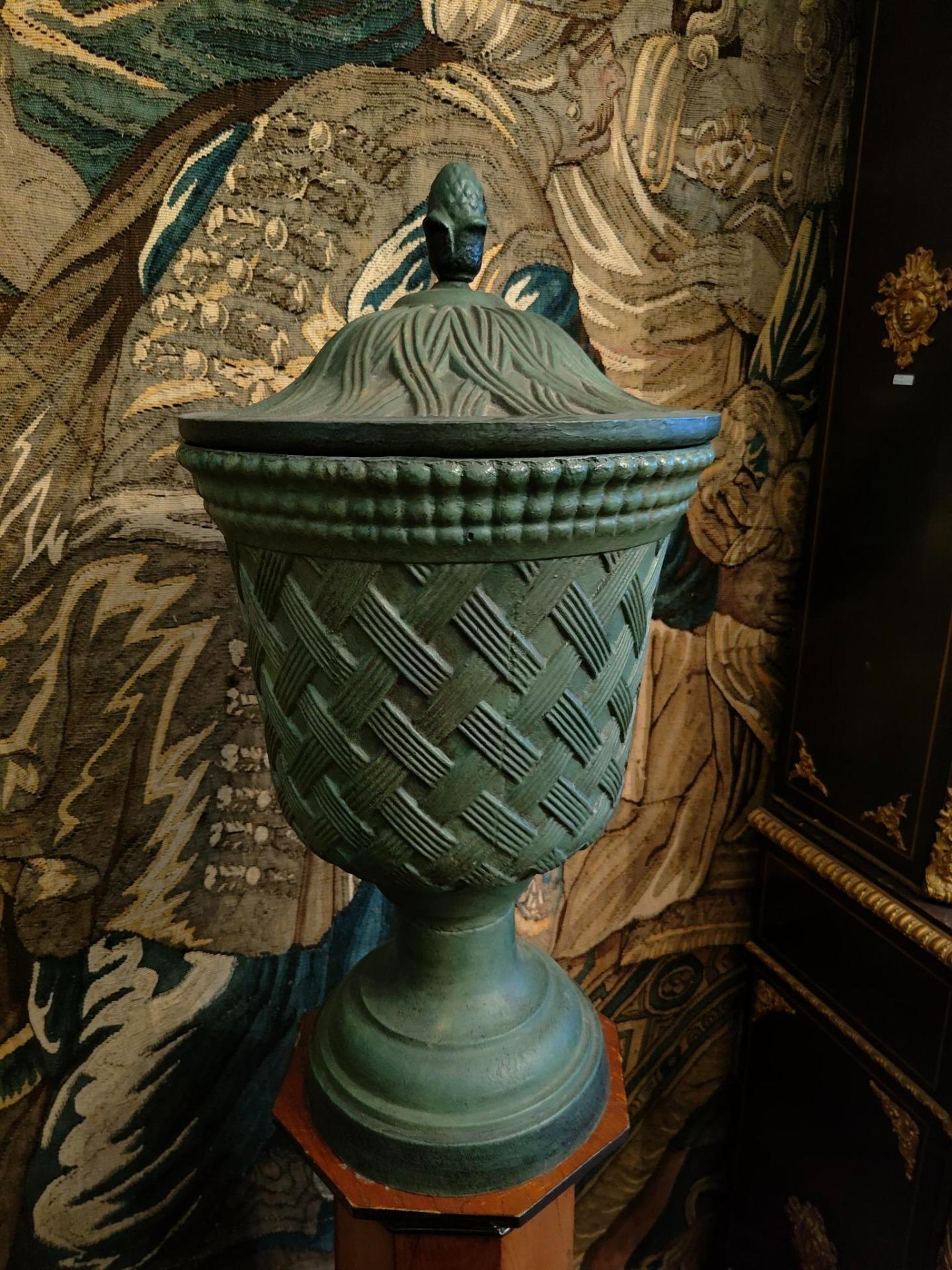 Belle paire de vases en fonte avec couvercles, soutenus par deux colonnes en bois.
Dans le corps des vases et le couvercle, le dessin imite une trame que l'on trouve habituellement dans des objets d'une autre nature, une trame typique de matériaux