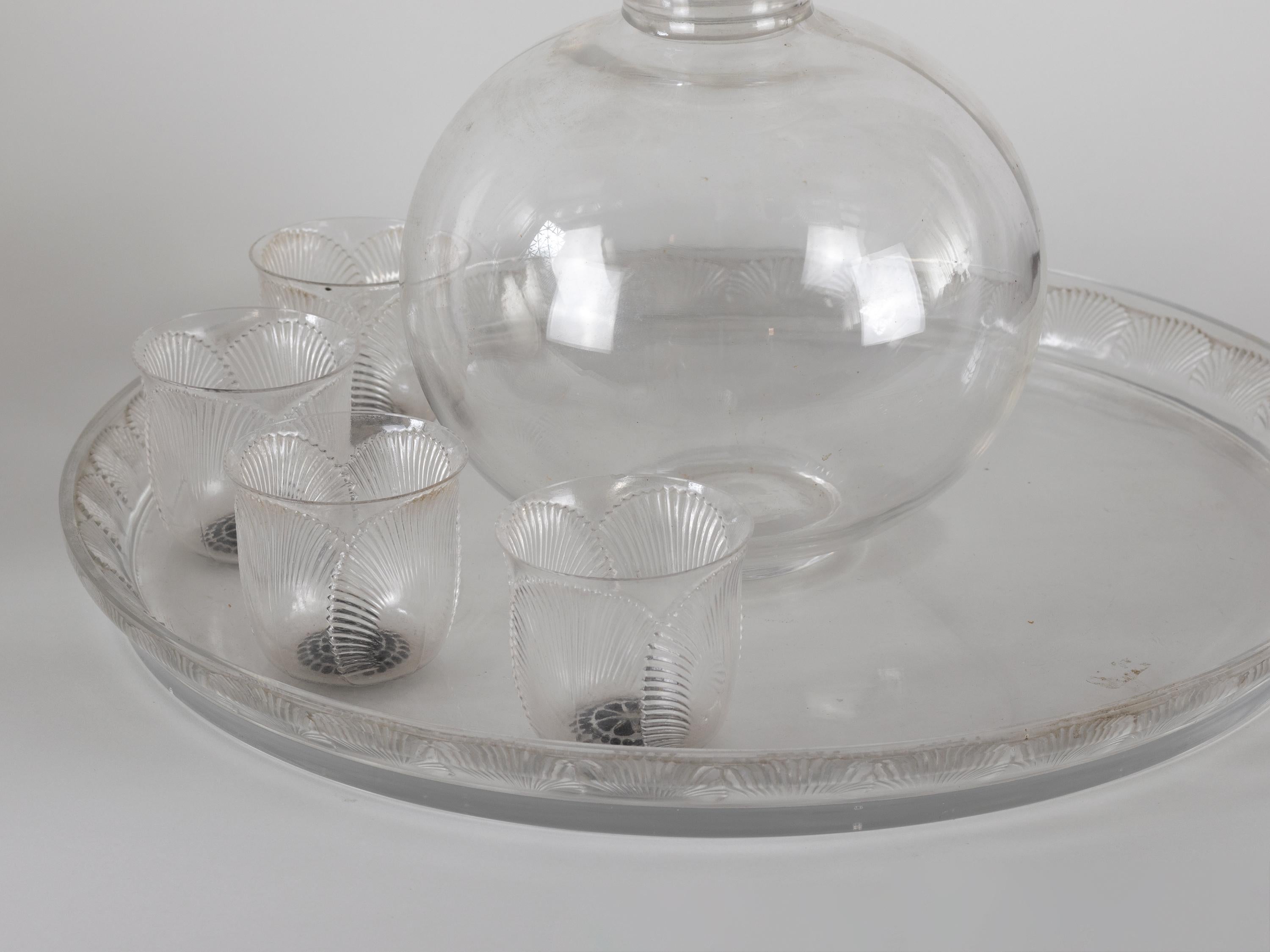 A 'Coquelicot' set of white blown glass, highlighted shells decorated matching model clear and frosted glass patina and enamel decanter, four glasses and one large plate.
“René Lalique” signed. 
Model created on May 8, 1930.
Decanter - model number