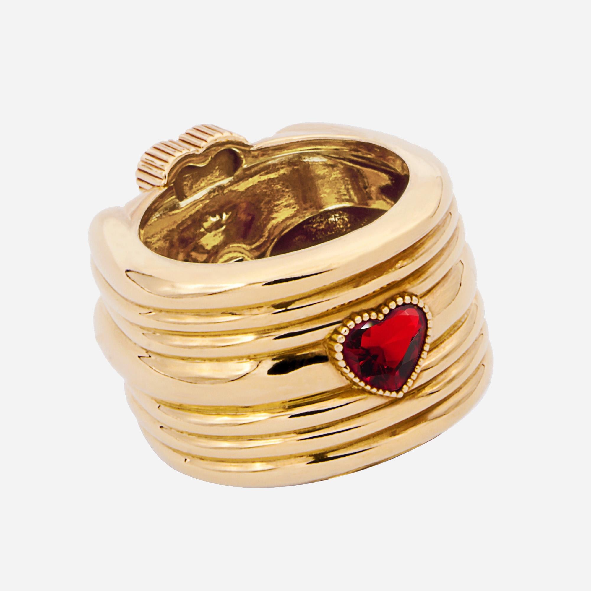 This ring is defined by an enveloping design and it is finished by a butterfly knurled pattern. On the top, it is embellished with three heart – cut red crystals.
In the lower part, it presents a small heart-cut red crystal that recalls the logo of