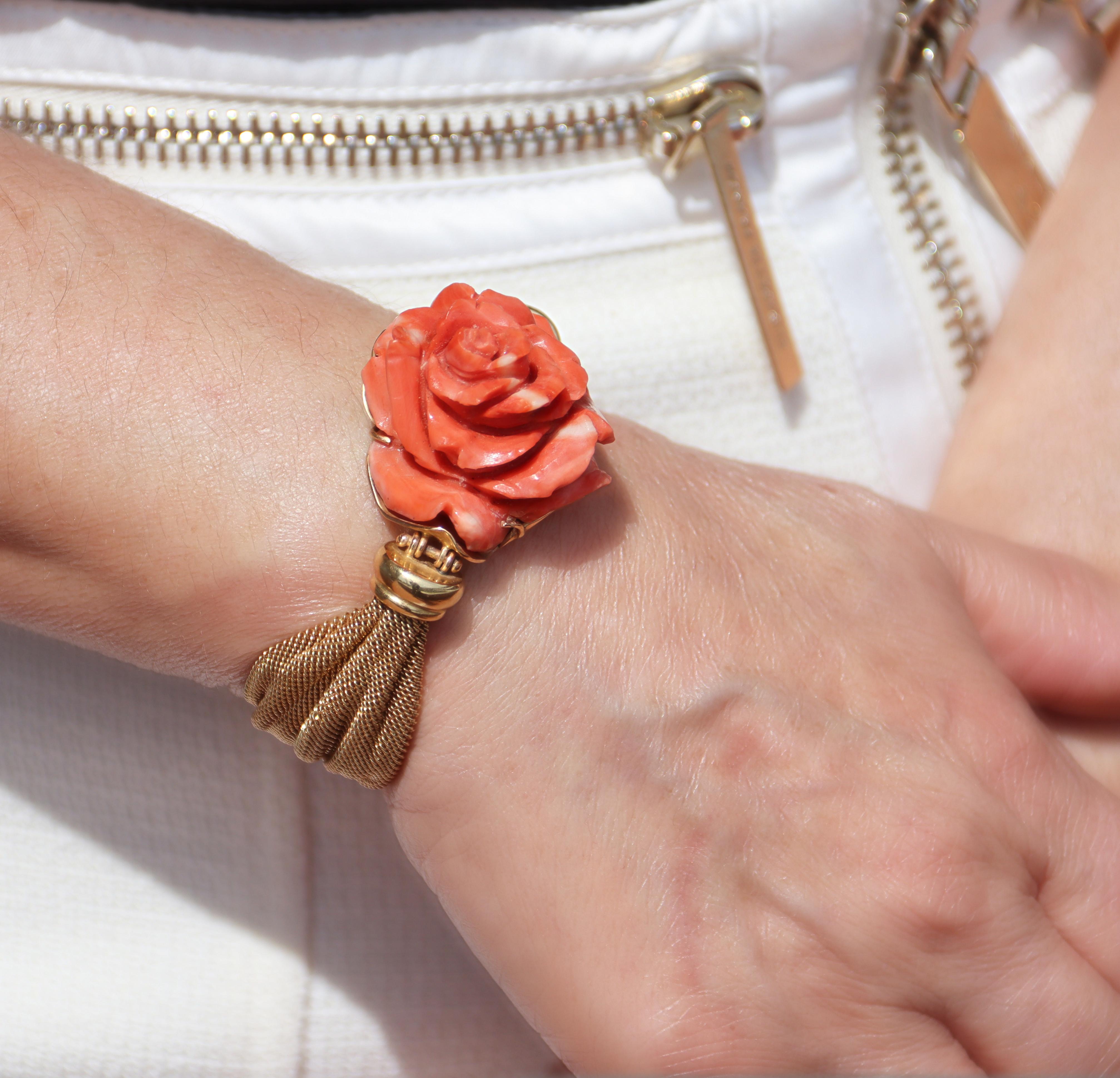 Capturing the essence of romantic elegance, this bracelet showcases a delicate 14-karat yellow gold mesh design, gracefully leading to its centerpiece, a meticulously sculpted natural coral rose. The rose, with its petals unfurled in full bloom, is