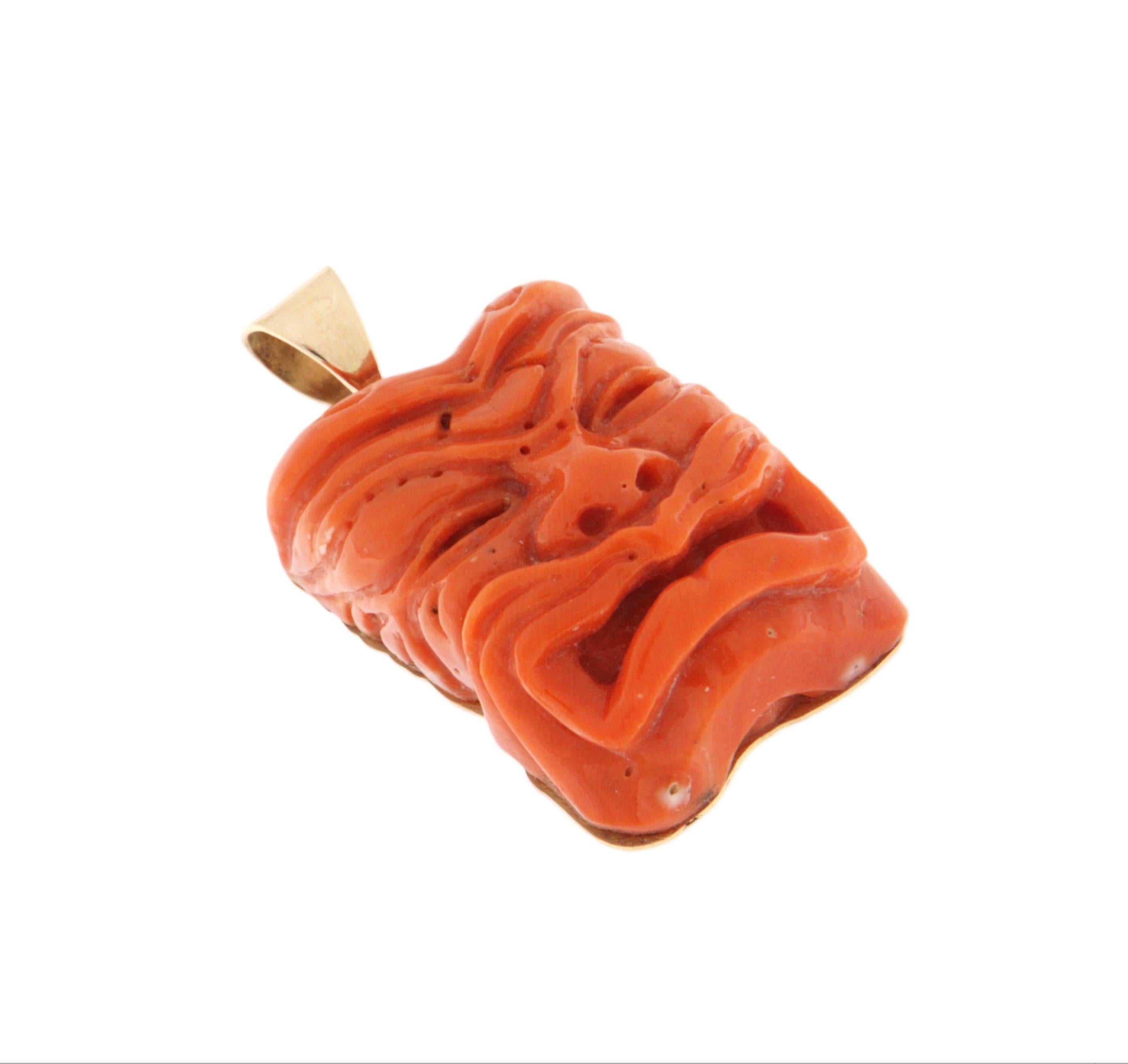 A fascinating handcrafted pendant in 14-karat yellow gold, featuring a finely carved natural coral sculpture depicting an expressive and mysterious mask. This is a unique piece, full of character, that combines the symbolic power of the carved face