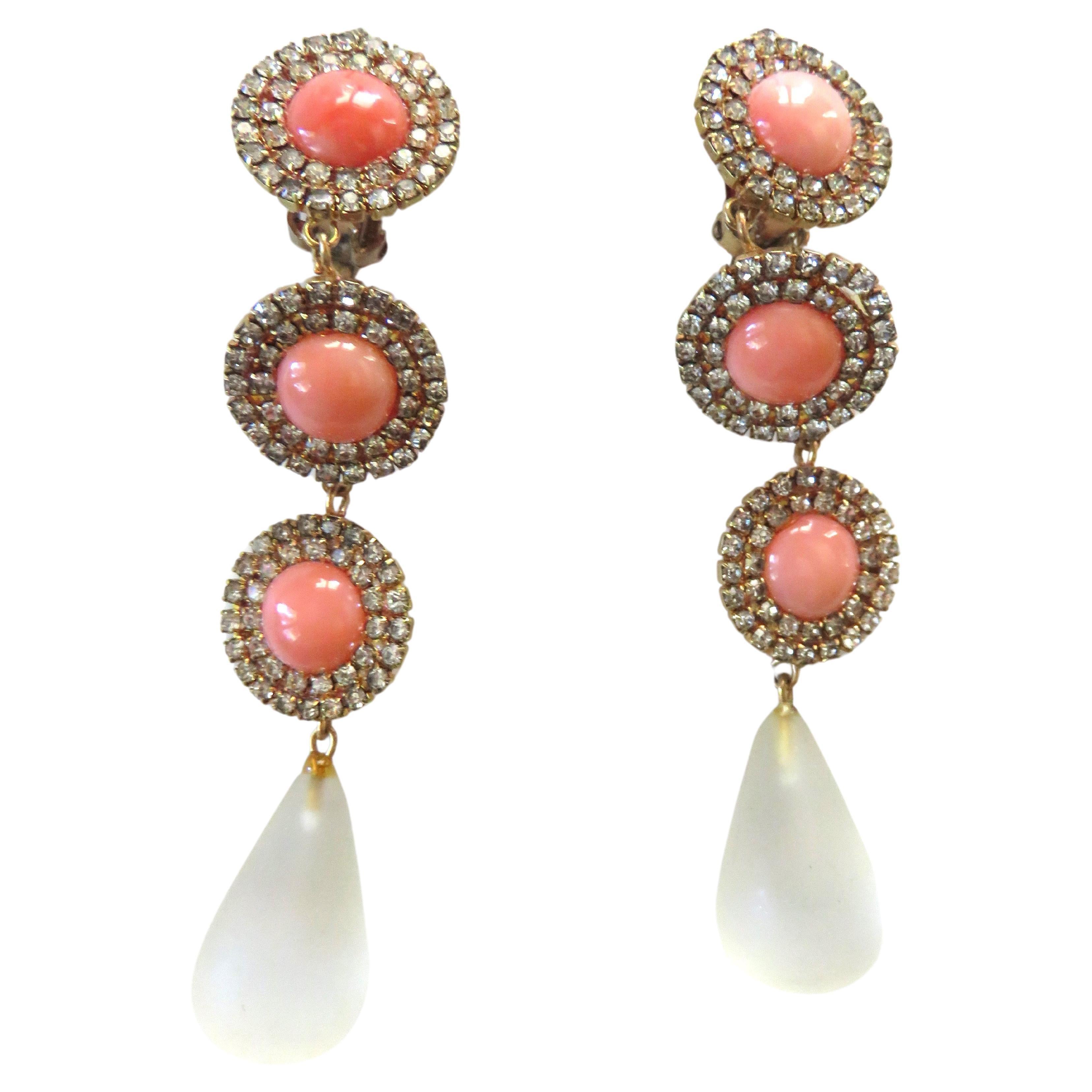 Splendidi orecchini a goccia in corallo e cristallo. Sono orecchini a clip composti da 3 coralli rotondi circondati da 2 file di cristalli brillanti. Una goccia di vetro smerigliato a forma di lacrima completa la parte inferiore dell'orecchino.