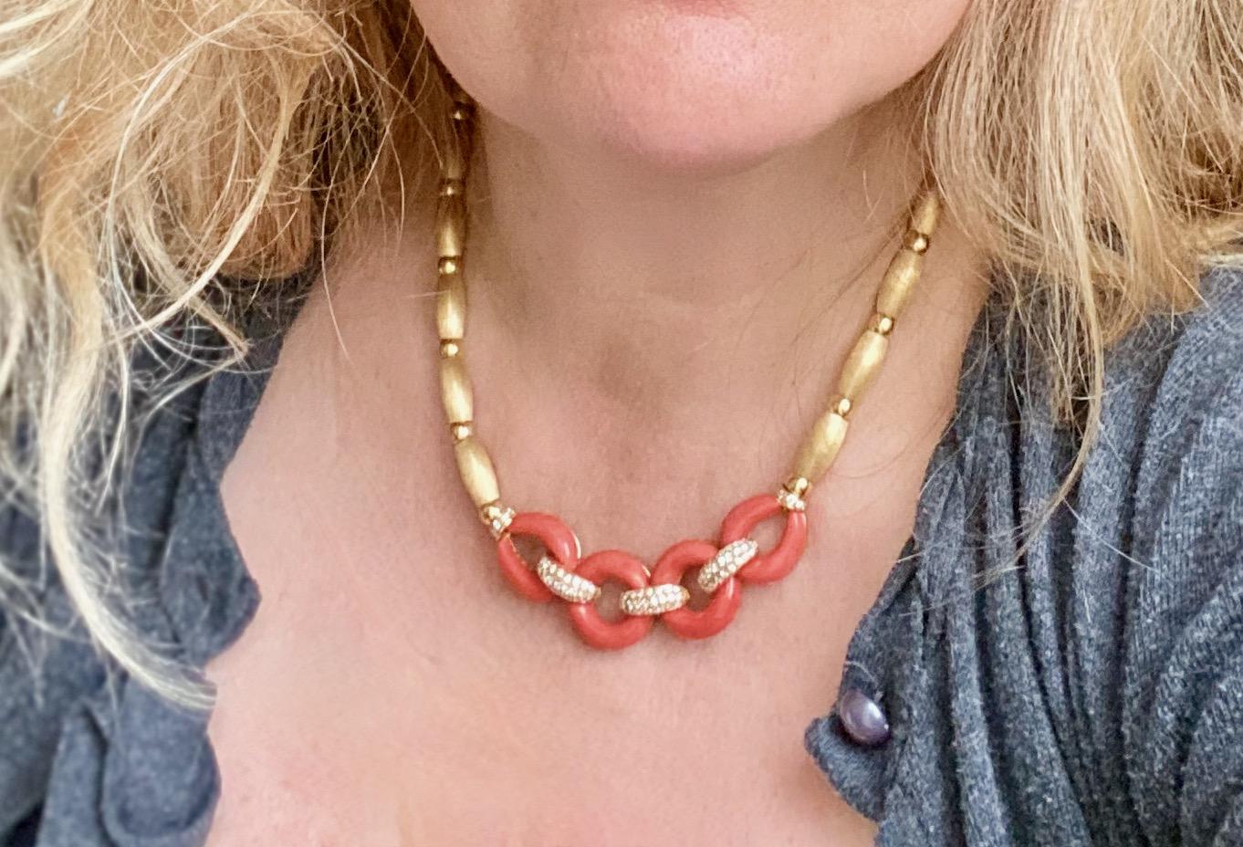 Coral and diamond brushed 18 kt Yellow gold necklace. It is composed of an 18 kt yellow gold chain threading alternating balls of curved tubes in brushed yellow gold retaining in its center two circles and two oval patterns of coral held between