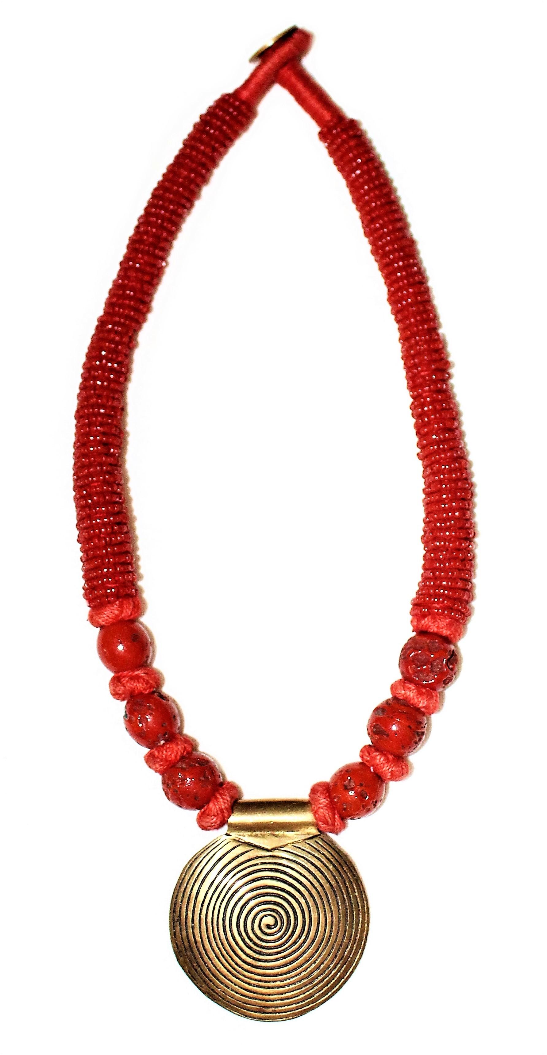 Circa 1970s to 1980s coral bead necklace with a large brass disk pendant.  The necklace is hand-tied together with coral-color thread and a looped thread clasp with a brass coin closure.  The necklace measures 17.5