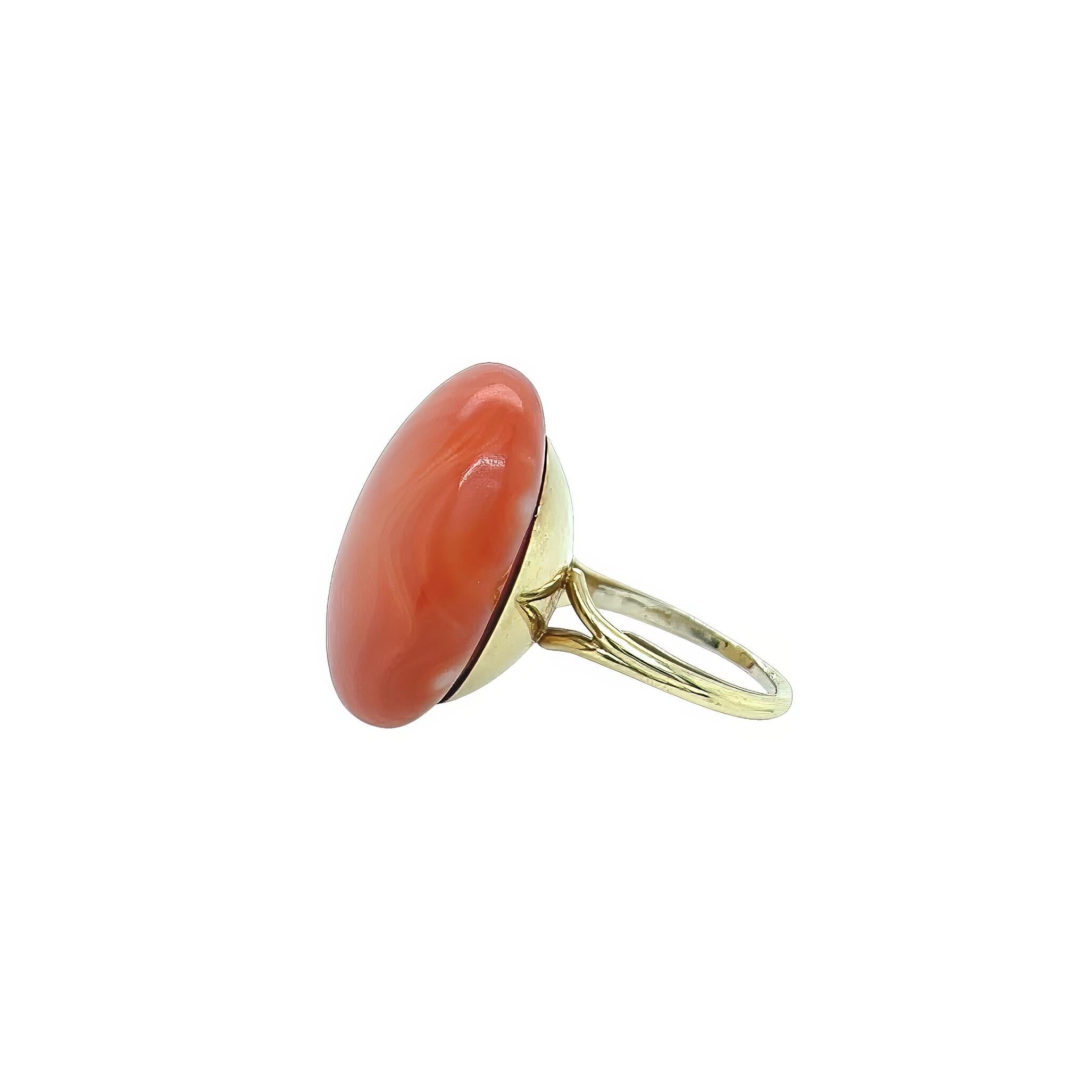Un anello in oro giallo 14 carati e corallo.  Disegnato come un corallo cabochon rotondo in una montatura a piatto sopra le spalle spaccate.  Taglia 5 circa.  Peso lordo di circa 15.40 grammi.