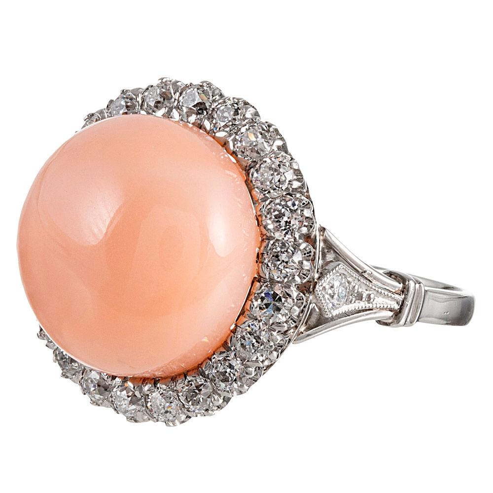 A 19.5 millimeter cabochon of coral is encircled by 1 carat of old European cut white diamonds, this classic style offering a unique twist with the coral centerpiece. Note the sculpted shoulders and filial decorations adorning them. The platinum