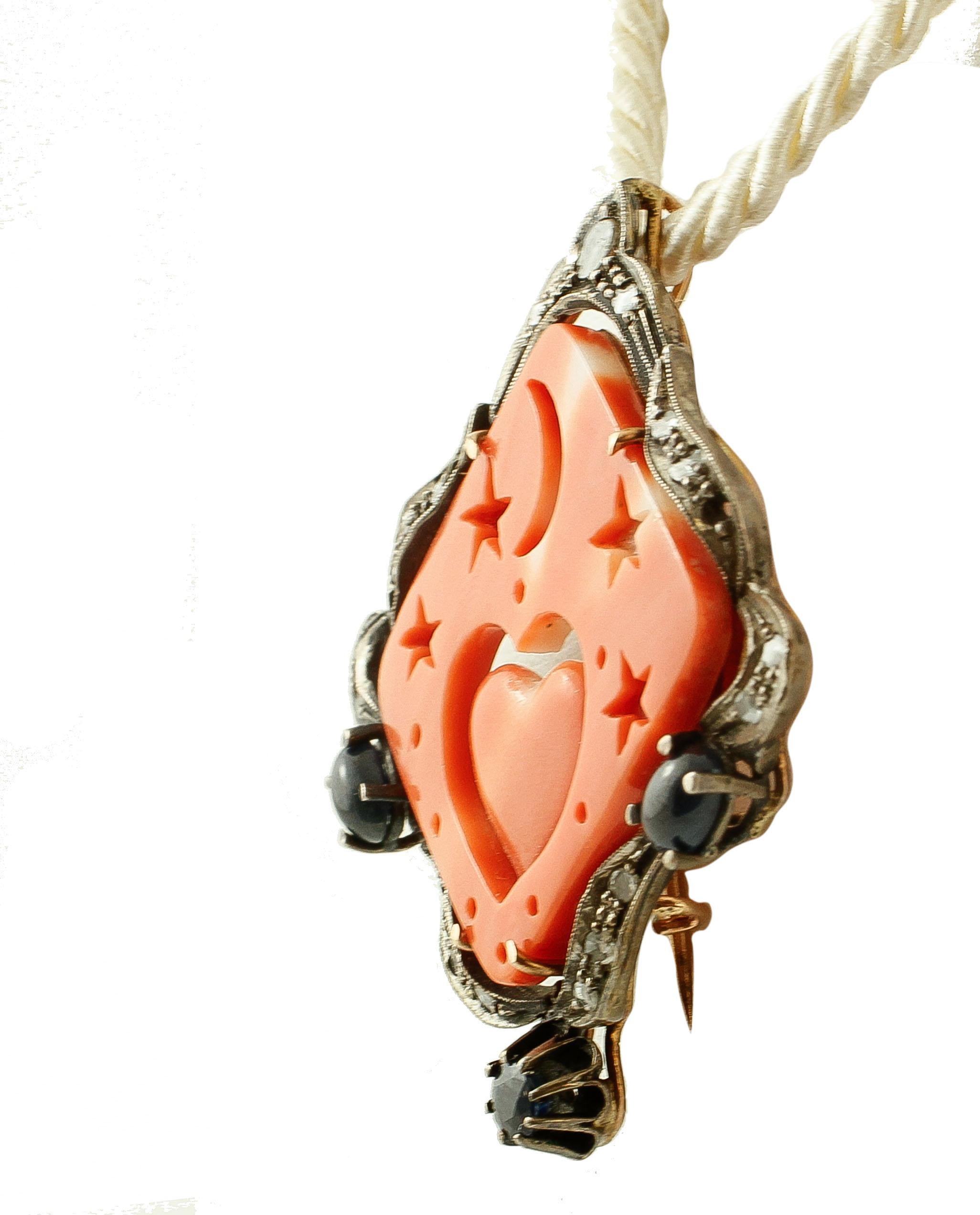 Beautiful pendant/brooch consisting of  a rhombus elatius coral, finely carved with stars, moon and heart motifs, and surrounded by a frame in 14k rose gold and silver structure enriched with diamonds and blue sapphires. 
This particular