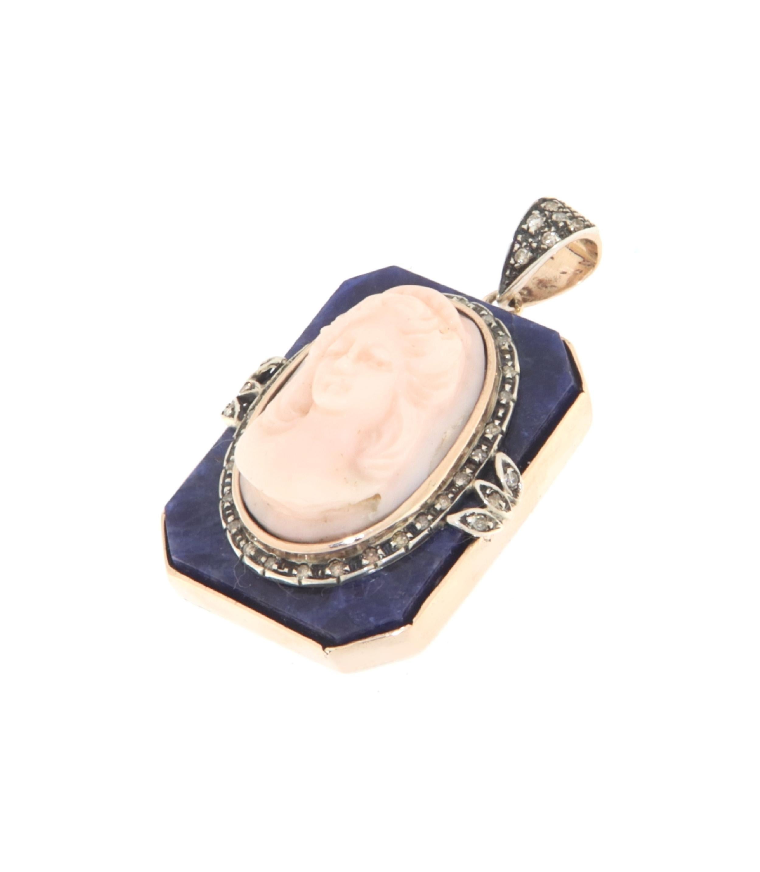 Ce magnifique pendentif combine avec élégance l'or 9 carats, l'argent 800 millesimi, le corail, les diamants et le lapis-lazuli en un bijou à couper le souffle. Il est orné d'un camée en corail magnifiquement sculpté représentant un visage serein,