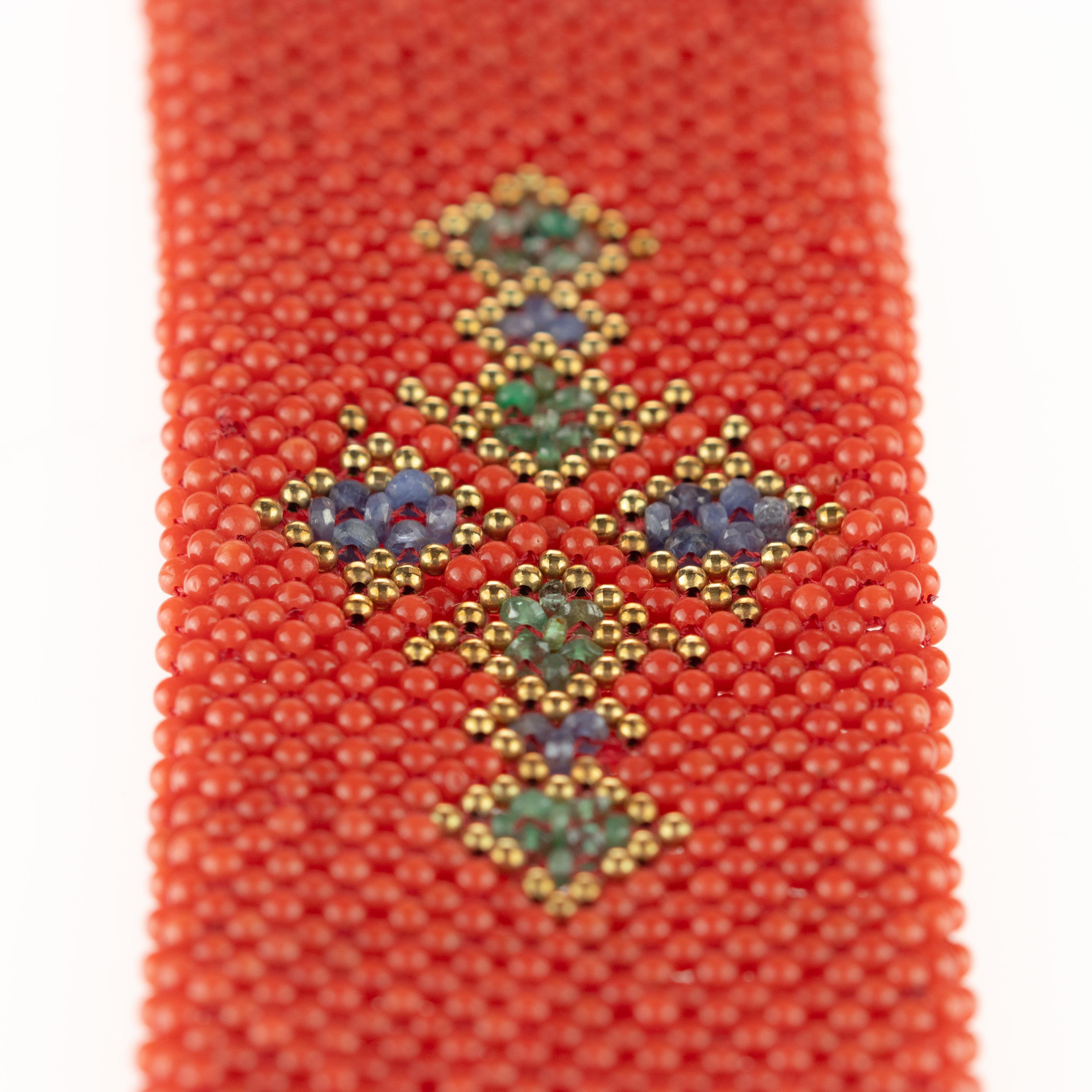 Iconico e straordinario bracciale tribale di perline intrecciate con un design a forma di croce/diamante. Corallo rosso impreziosito da smeraldi e zaffiri e da un fermaglio in oro giallo 18 carati.
 
Questo accessorio di gioielleria è ispirato alla