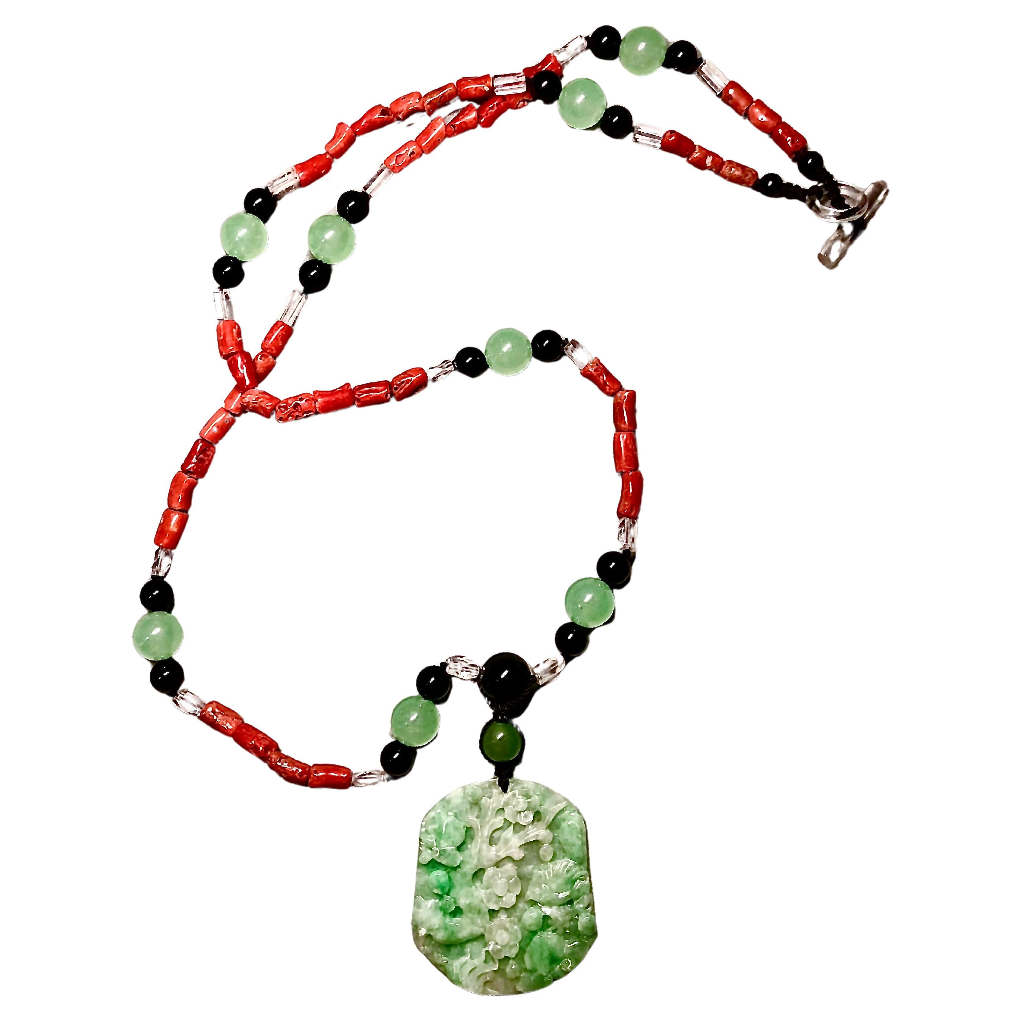 Striking combination of natural red Sardinian coral with stations of luminous green jade round beads flanked with round black onyx beads and faceted tubes of rock crystal. Suspended from the beads is a green mottled jade well carved plaque. The