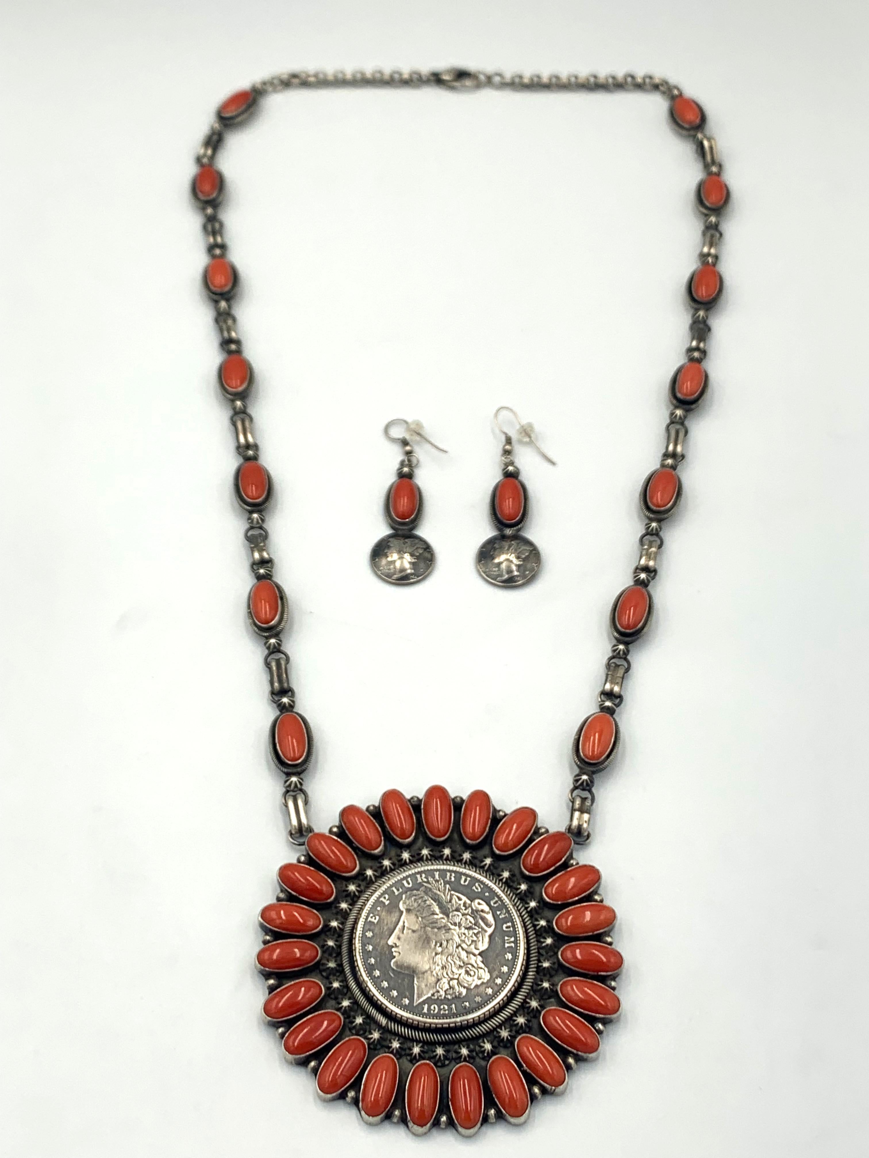 Coral necklace with a silver dollar centerpiece by Navajo silversmith Paul Livingston. The 3 ¼” x 3 ¼” coral pendant has 23 coral cabochons showcasing a 1921 Morgan silver dollar. Fourteen Coral cabochons are spaced between the links of the 26”