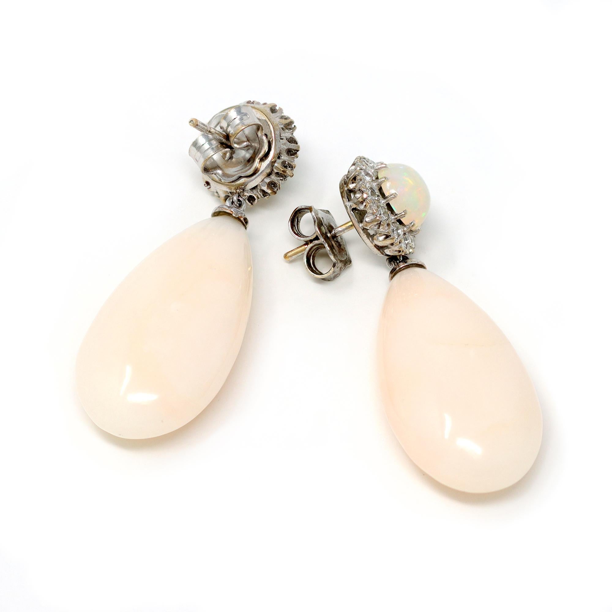 A one-of-a-kind dangling earrings featuring light pink coral drops dangling from a round opal stud surrounded by a halo of diamonds. The earrings are set in 18-karat white gold; they are vintage, circa 1960-70. The hallmarks read S&R. The diamond's