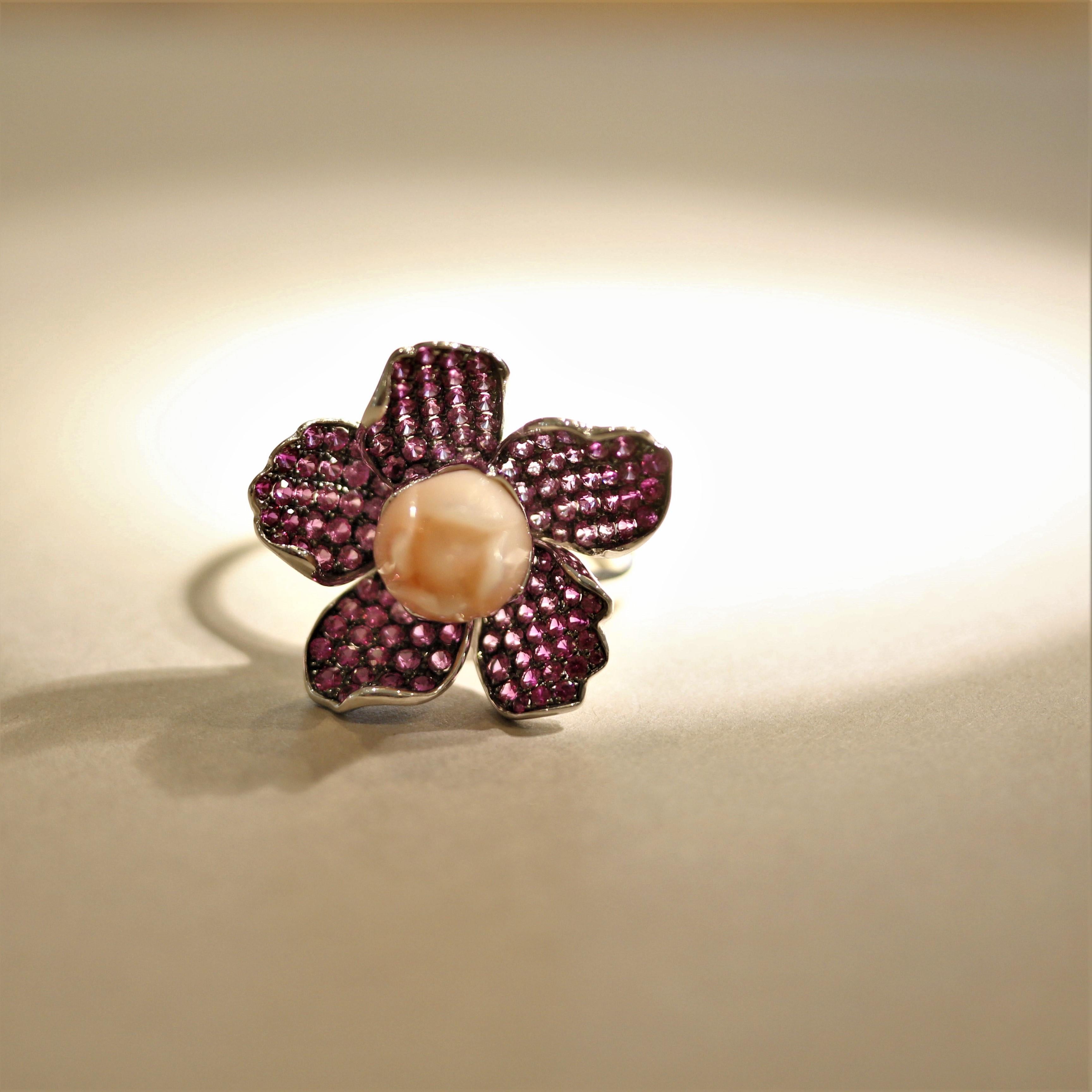A sweet and stylish flower ring! It features a fine piece of coral which has been hand-carved into a blossoming flower. It is accented by 2.22 carats of bright hot-pink sapphires which are set as the flower’s petals. Made in 18k white gold with