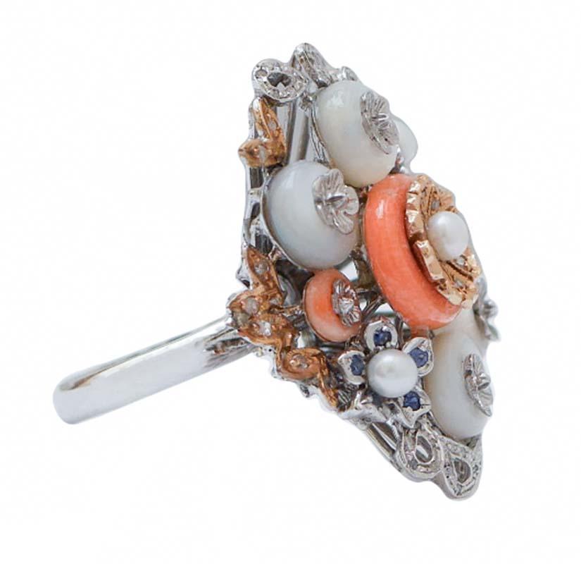 Bague fantaisie en or blanc 14 kt structure montée avec  coraux, perles et pierres blanches entre des feuilles et des fleurs serties de diamants et de saphirs.
Cette bague a été entièrement réalisée à la main par des maîtres orfèvres italiens et