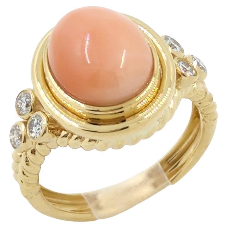 The ring showcases an oval coral gemstone with a salmon color, creating a vibrant and eye-catching centerpiece.

On each side of the ring's shoulder, there are three diamonds set to add a touch of sparkle and elegance. These diamonds, with a total