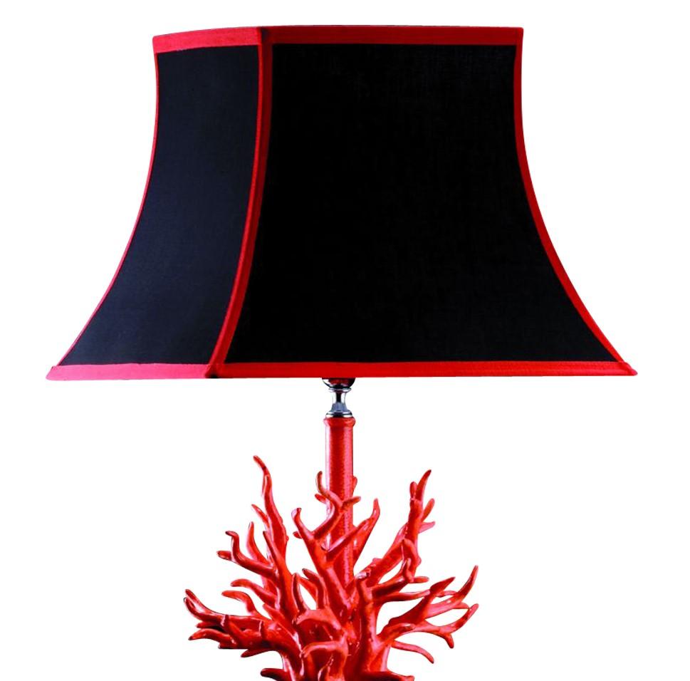 This striking desk lamp features a black geometric stand adorned at the top with a ceramic decoration representing a vivid red coral branch. The red accents appear also on the black shade with coral-colored details at the edges.