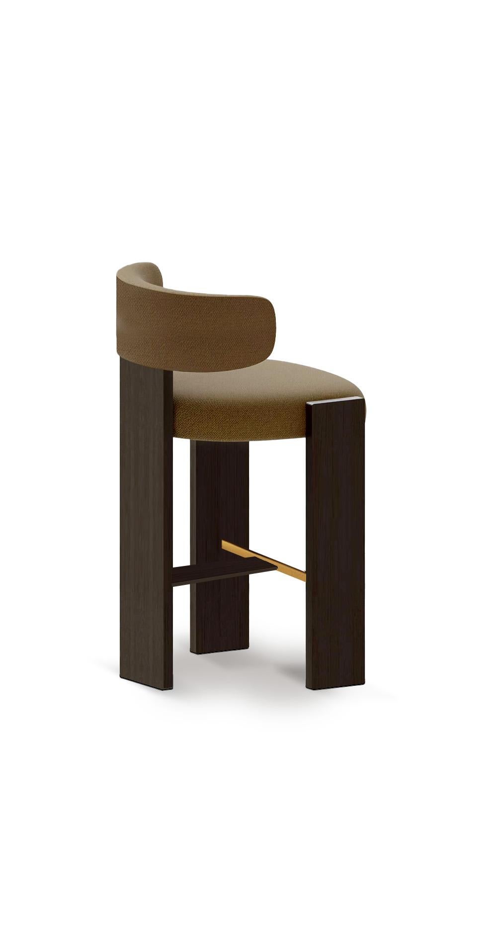 La sedia da bar Core unisce il rigore architettonico alla morbidezza scultorea. Con la sua robusta struttura geometrica in Oak e lo schienale imbottito dolcemente curvo, offre struttura e comfort. Il dettaglio del poggiapiedi in ottone aggiunge un