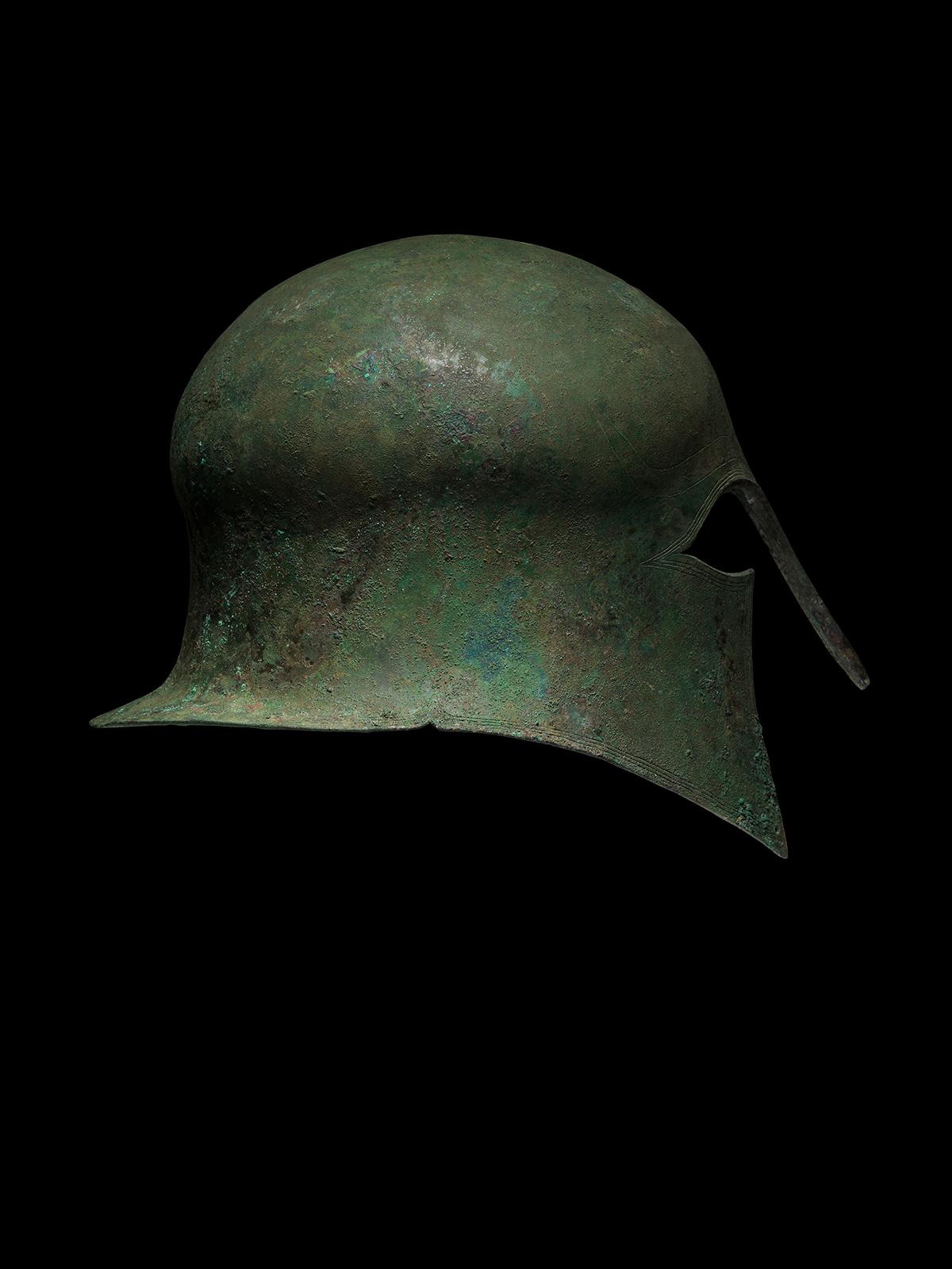 A bronze helmet made of a single hammered bronze plate in the characteristic shape of the military Corinthian type helmets of the end of the 7th century and the beginning of the 6th century B.C.. The type is defined by the characteristic