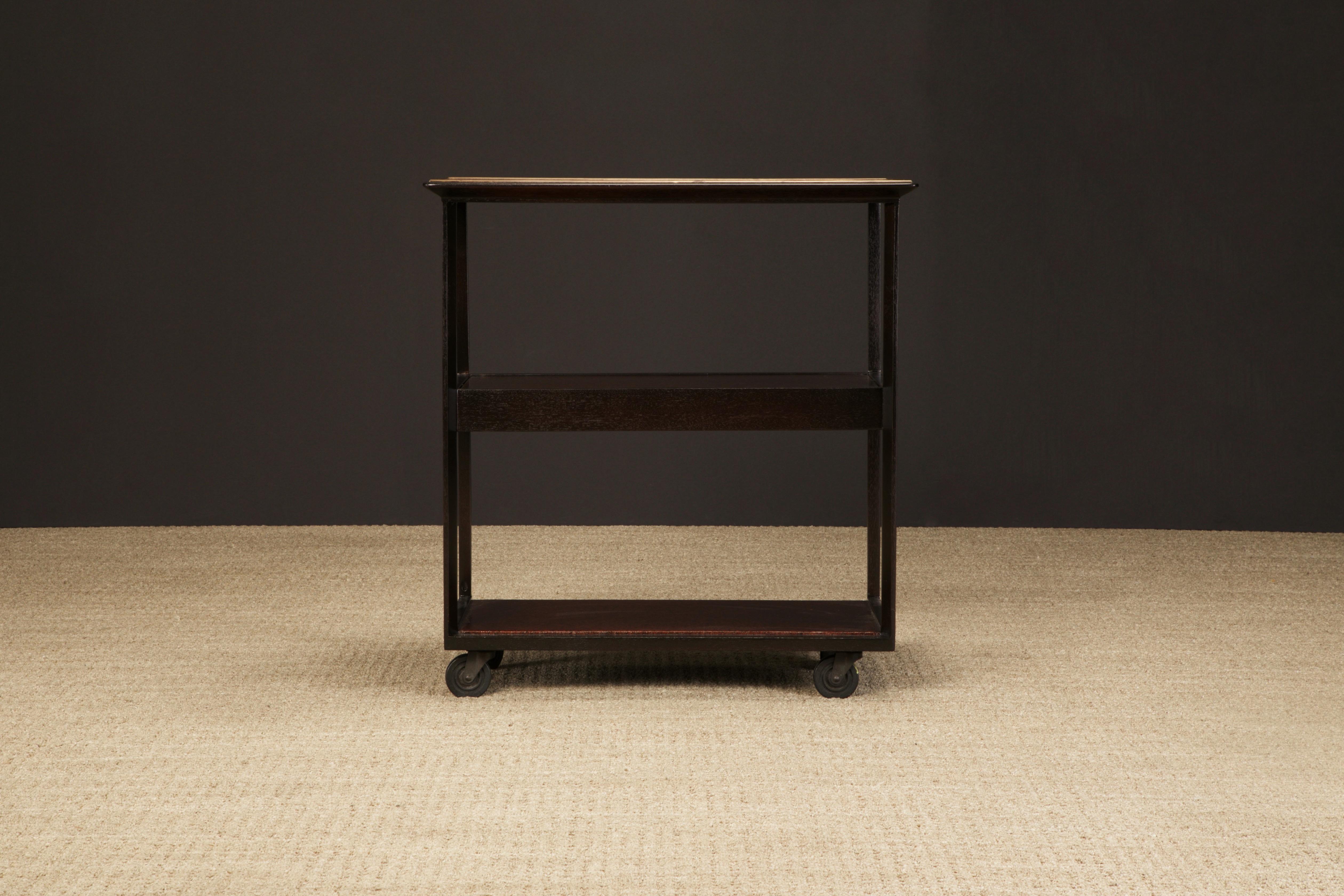 This classic Edward Wormley for Dunbar bar cart, circa 1960s, features a cork top with brass trim and the two lower platforms also with cork, a hidden drawer to stow away your goodies and on casters for ease of relocation. We just completed