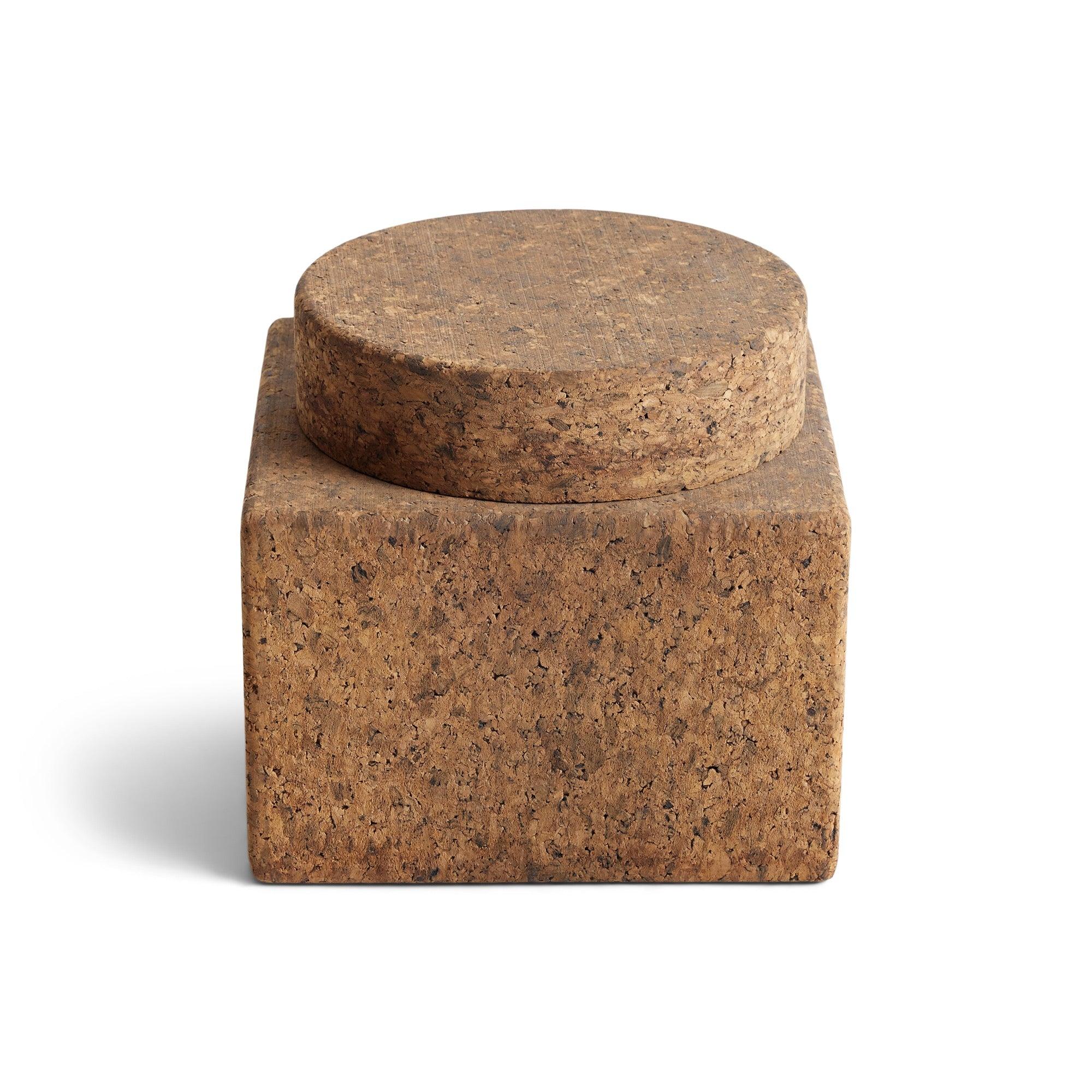 An ice bucket by Mort Morton with a cube base and round lid all made of solid cork with a porcelain insert.