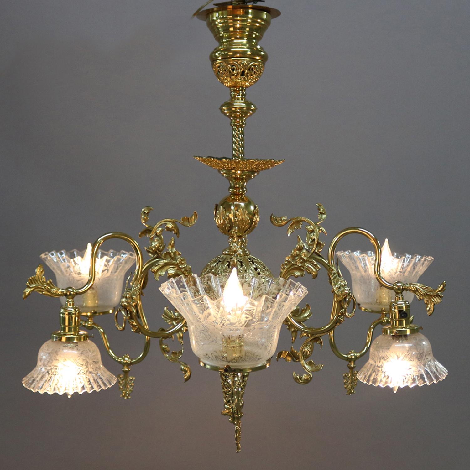 Cornelius School chandelier features gilt cast white metal frame with central pierced foliate drop finial and font with six scroll and foliate form arms terminating in up and down independently controlled lights having foliate etched shades with