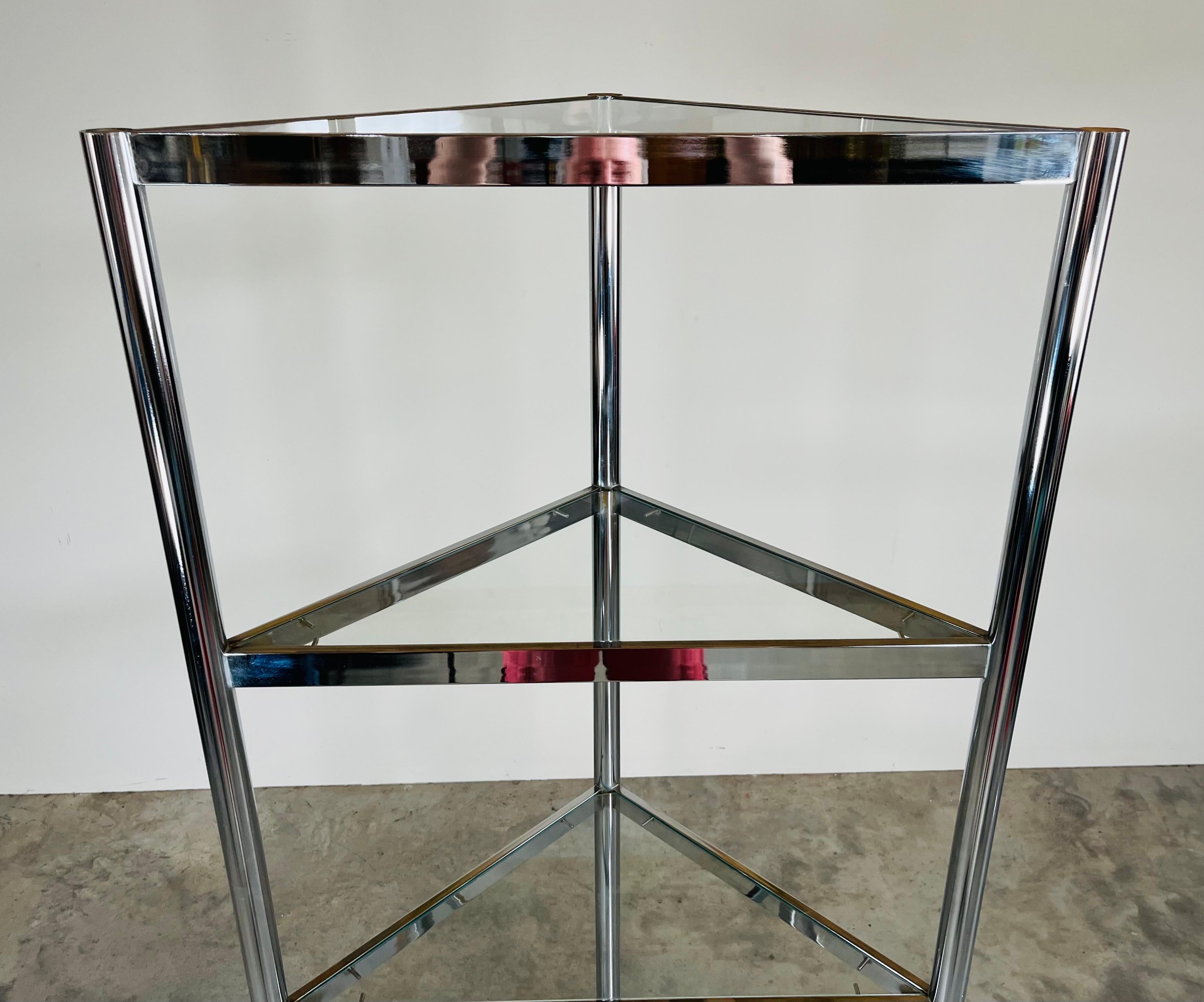 Espositore triangolare alto in vetro e cromo nello stile di Milo Baughman. Cinque ripiani, compreso quello superiore.
In eccellenti condizioni d'epoca, con il vetro intatto e alcune piccolissime macchie sulla parete posteriore, ma nessuna sulla
