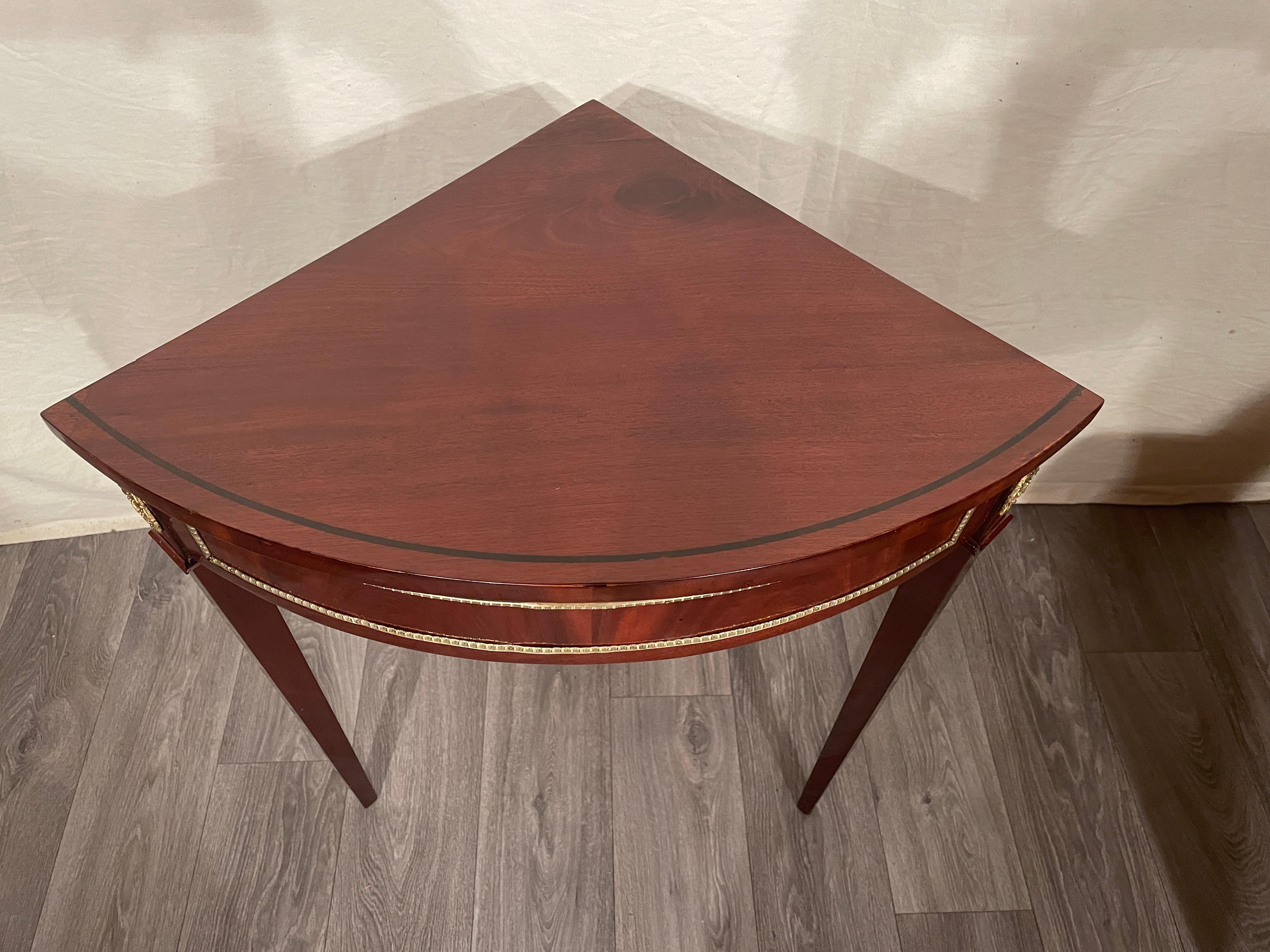 This elegant little Empire corner console table is embellished with mahogany veneer and pretty brass decorations. 
It is in very good, professionally refinished condition. The perfect little piece for any corner of your house or apartment.