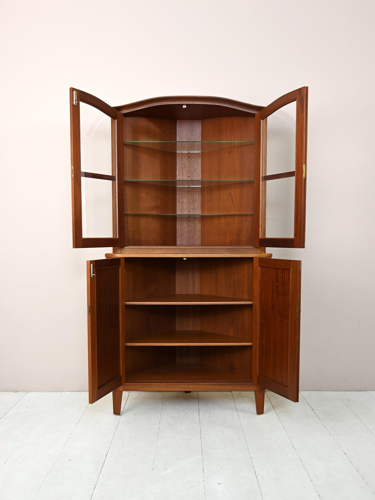 Vintage two-body teak corner cabinet.

An iconic Scandinavian 1960s design furniture piece.
The lower part is a storage compartment with hinged doors, and the upper part consists of glass shelving and is closed by a lockable cabinet.
Sophisticated