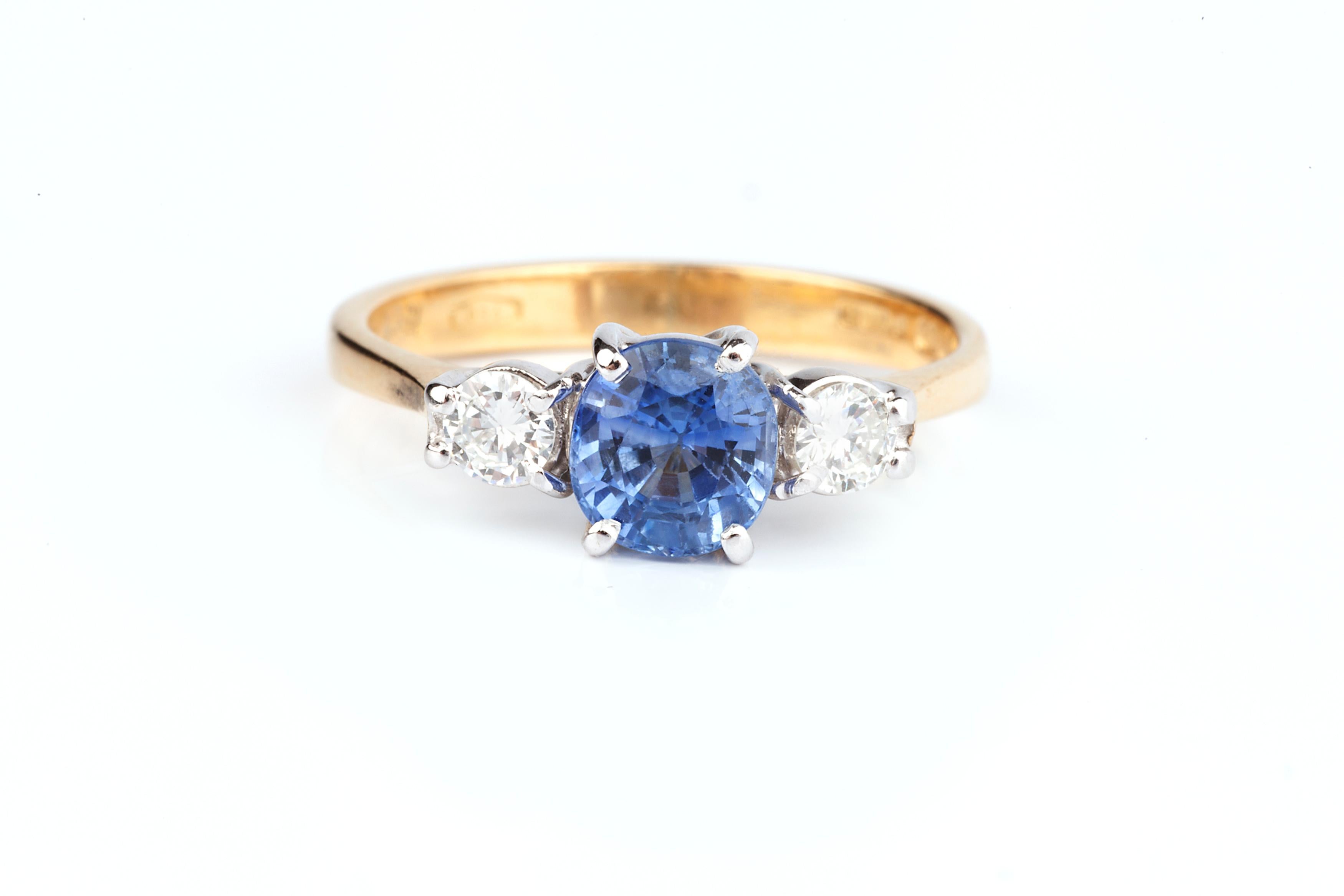 A cornflower blue sapphire and diamond trilogy ring, set with a central cornflower blue sapphire which is eye clean beautiful stone and two diamonds totalling in 0.3cts VS2 clarity. It is set in 18 karat gold and fully hallmarked. This is a vintage