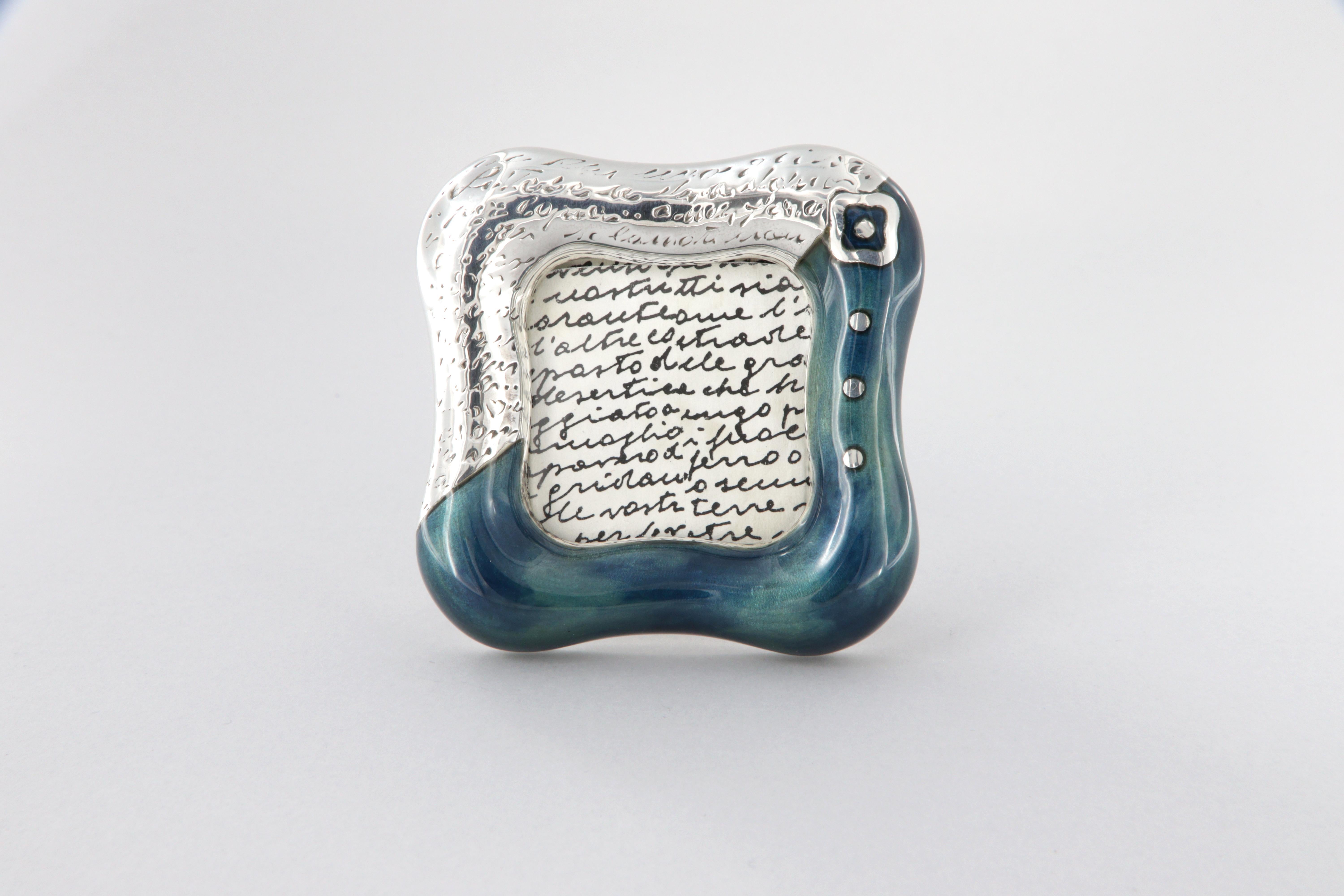 Cadre de bureau La Nouvelle Bague en argent 925/ooo et émail au feu bleu.
Dimensions 6 x 6 x 1,5 cm, poids total 60 g.
Ouverture de la photo cm 3,5 x 3,5
Fabriqué en Italie - Florence 1997

La forme particulière de la fleur carrée stylisée est